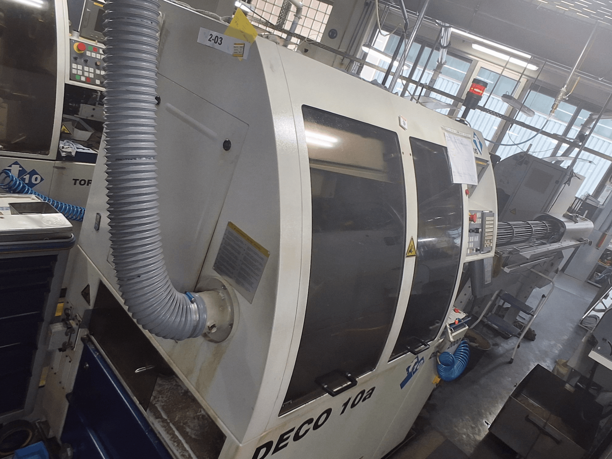 Máquina DECO 10a en una vista frontal; presenta un gran panel de control, conductos y adhesivos operativos visibles.