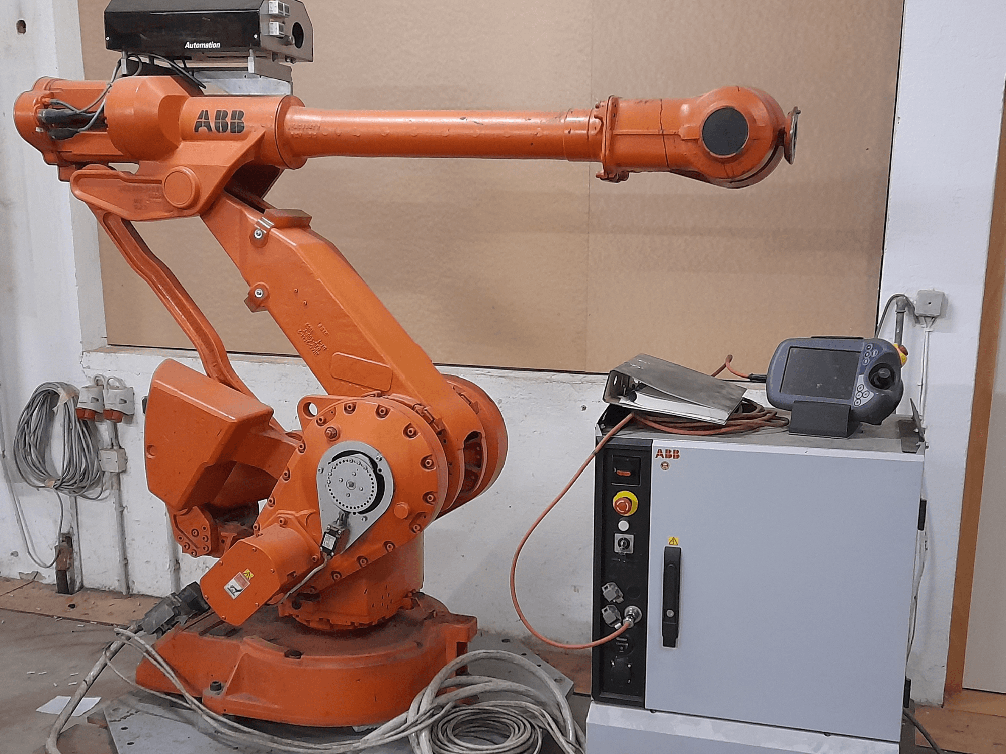 Brazo robótico ABB naranja con panel de control, vista frontal, mostrando cables y equipos de automatización.