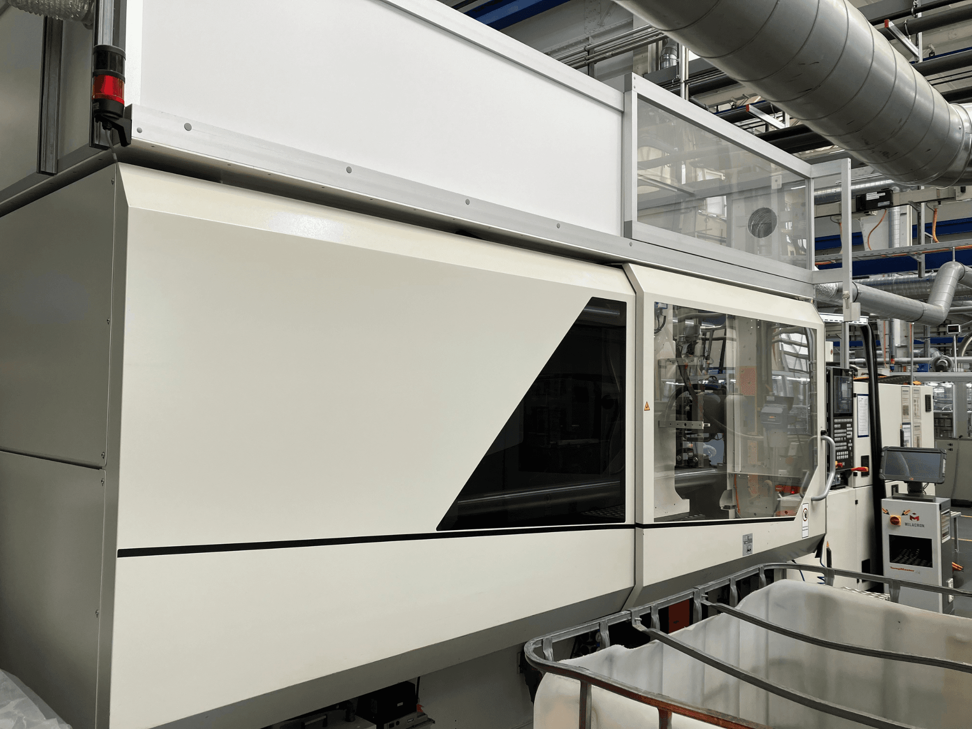 Vista frontal de la máquina industrial, con un elegante diseño blanco, panel de visualización y sección de cristal para la visibilidad de los componentes.