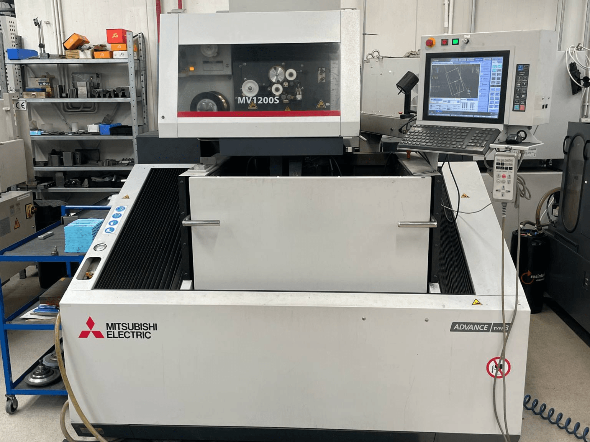Máquina de electroerosión por hilo Mitsubishi MV1200S vista de frente, en la que se aprecian el panel de control y la zona de trabajo, con las advertencias de seguridad visibles.