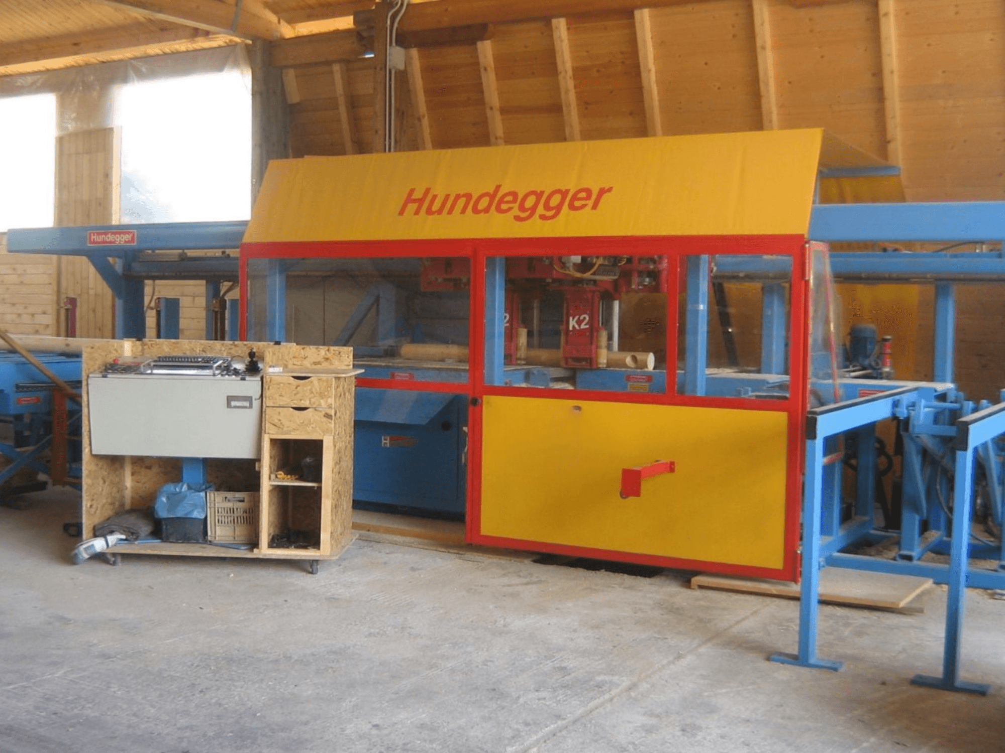 Centro de mecanizado de madera CNC HUNDEGGER K2 4 assi en un taller, vista frontal mostrando diseño amarillo y azul con mesa de trabajo.