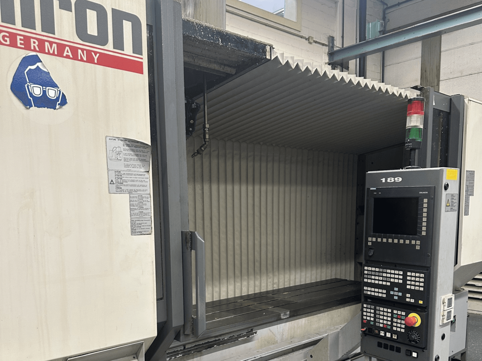 Texto alternativo: Vista frontal de una máquina CNC de Hermle con un panel de control que muestra botones y una pantalla, con un área de trabajo abierta.