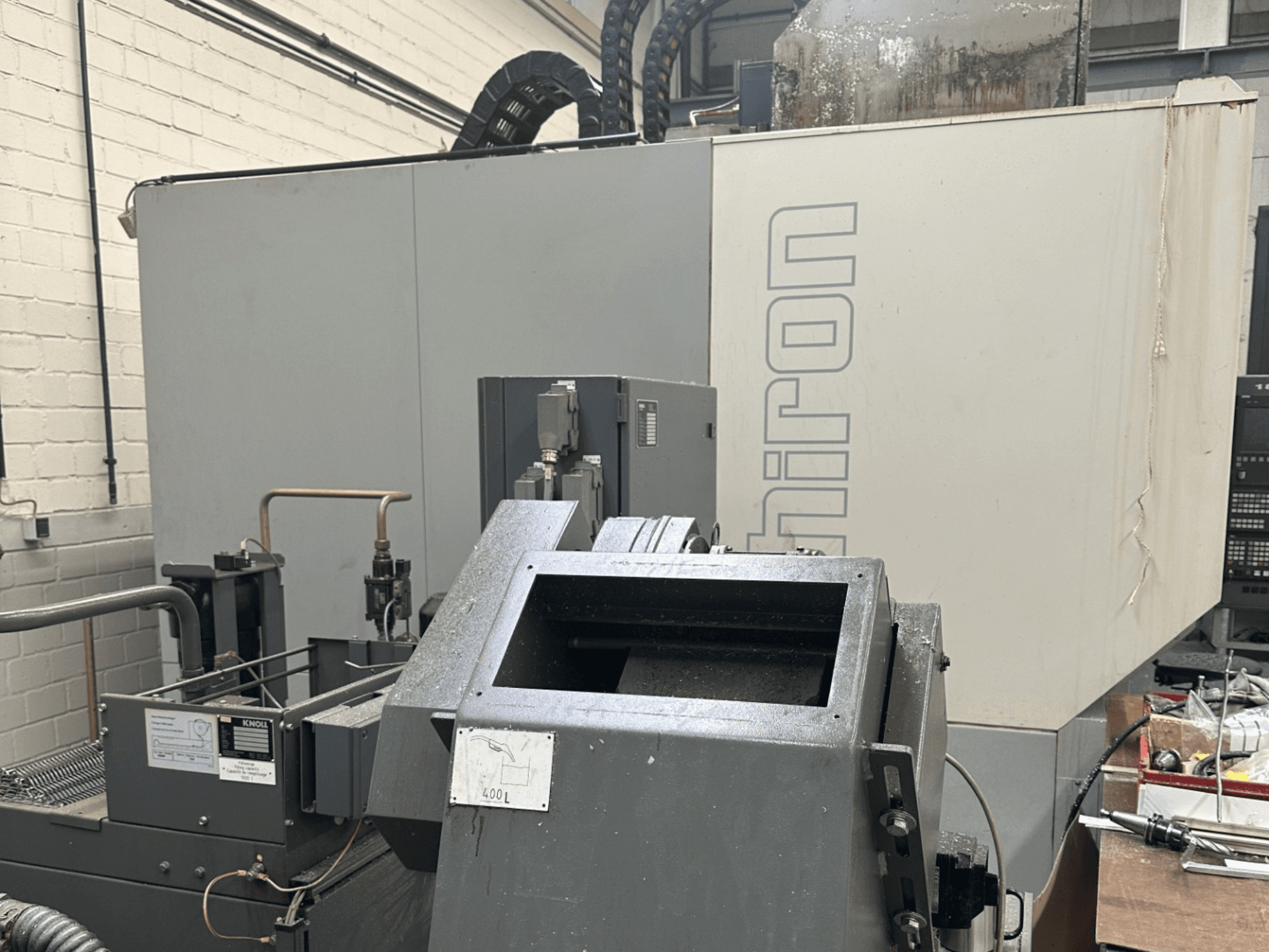 MARCA: Chiron; Vista frontal de máquina CNC industrial con exterior gris, panel de control visible y componentes de la maquinaria enfocados.