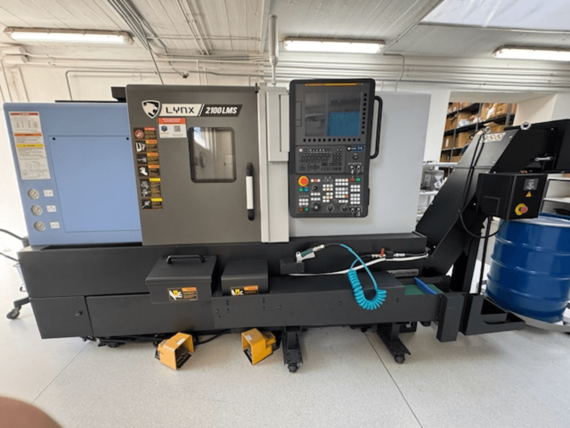 Máquina de torneado horizontal DOOSAN LYNX 2100LMSA, vista frontal, con panel de control, manguera de refrigerante y cajas de almacenamiento.