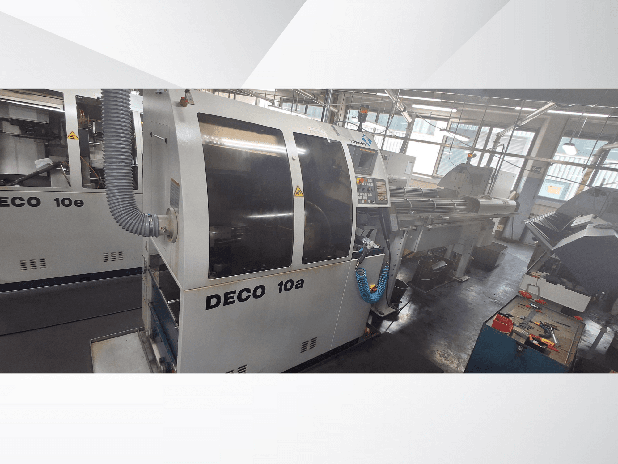 Máquina CNC DECO 10a en un taller, mostrando la vista frontal, el panel de control y el sistema de escape. Construcción robusta y herramientas de precisión.