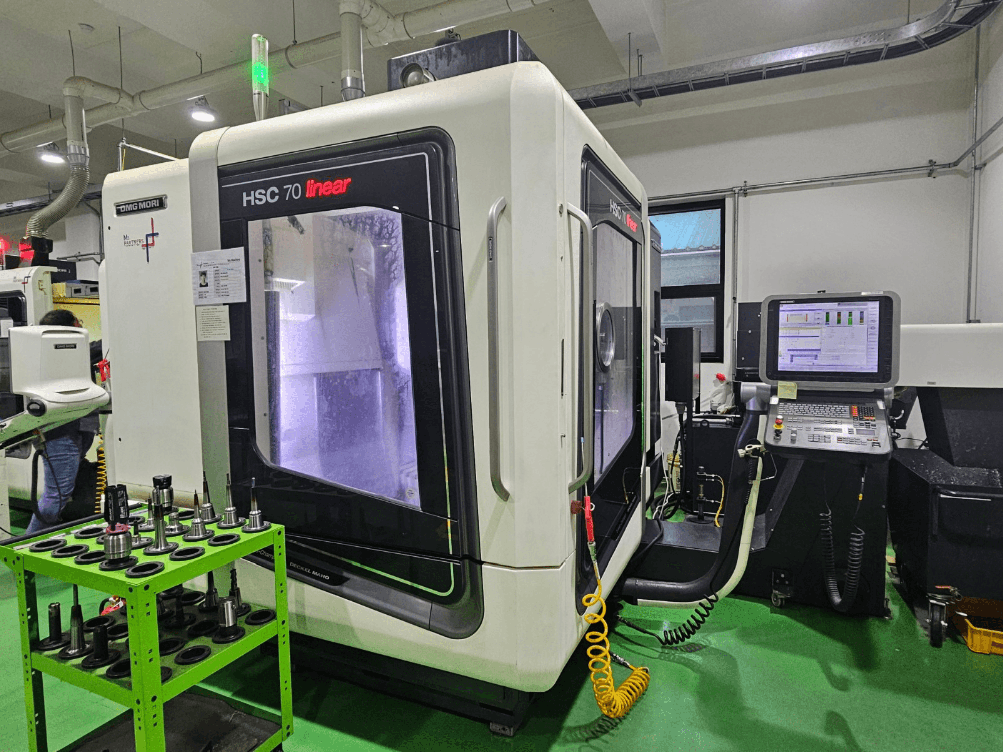 Centro de mecanizado universal lineal DMG MORI HSC 70, vista frontal, con portaherramientas sobre una mesa verde y un panel de control visible.
