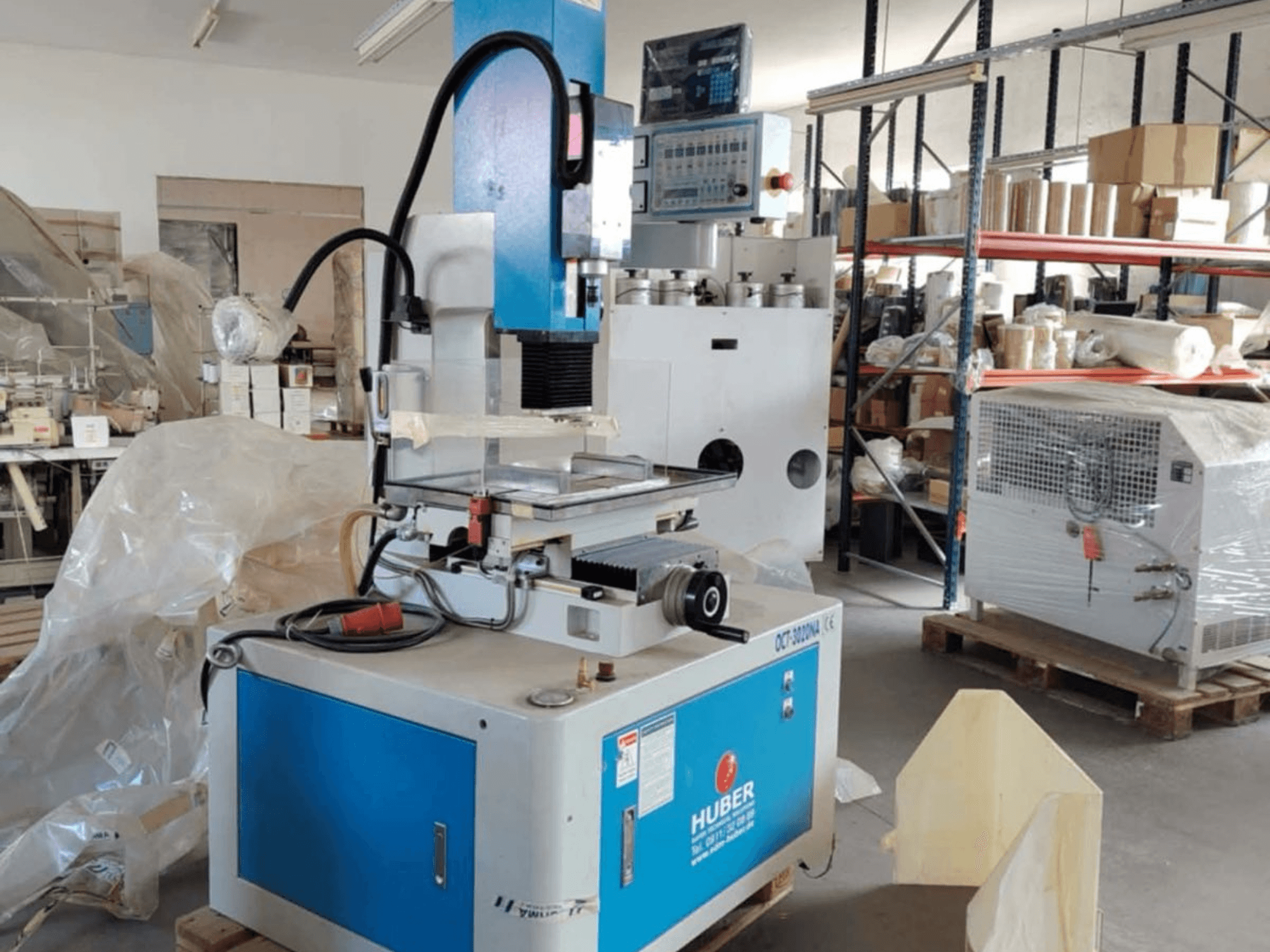 Máquina de electroerosión por penetración HUBER OCT-3020 NA en un taller, vista frontal que muestra la carcasa azul y gris, los controles digitales y el área de trabajo.