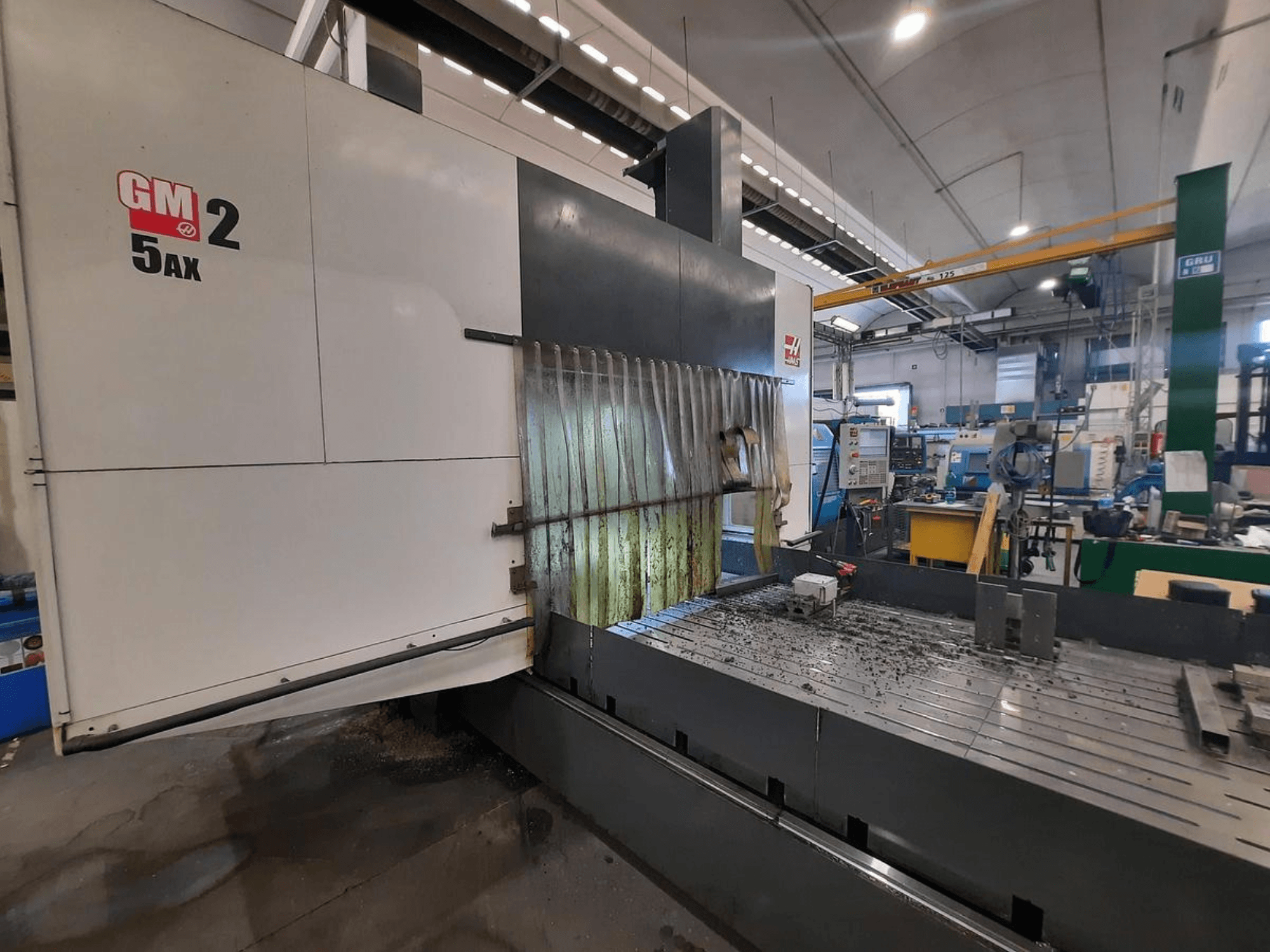 Máquina CNC GM 2 5AX en un taller, vista lateral, mostrando la zona operativa y las virutas de metal en la superficie de la bancada.