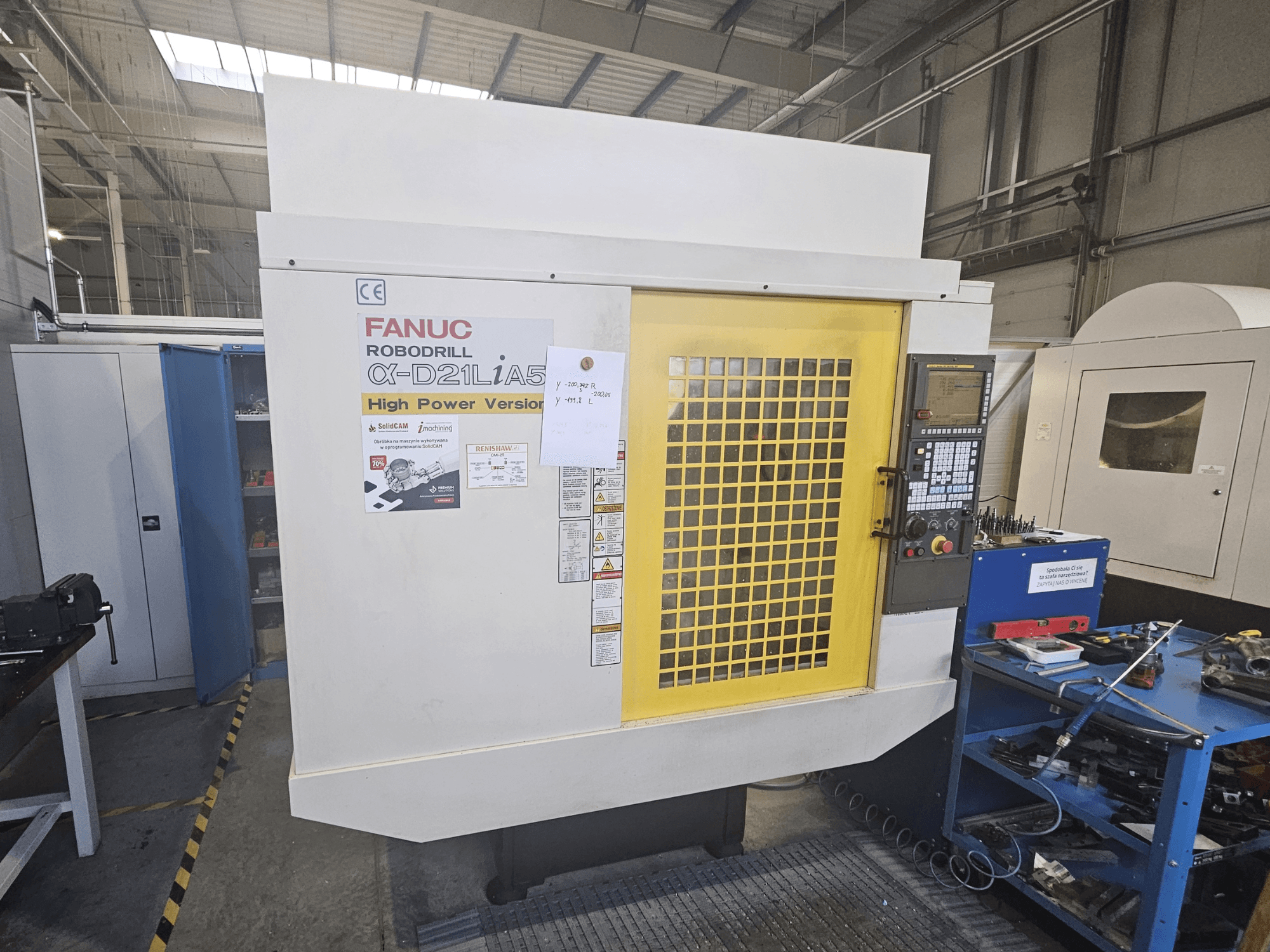 Vista frontal de una FANUC Robodrill α-D21LiA5 con la puerta de seguridad amarilla, el panel de control y las herramientas del espacio de trabajo cerca.