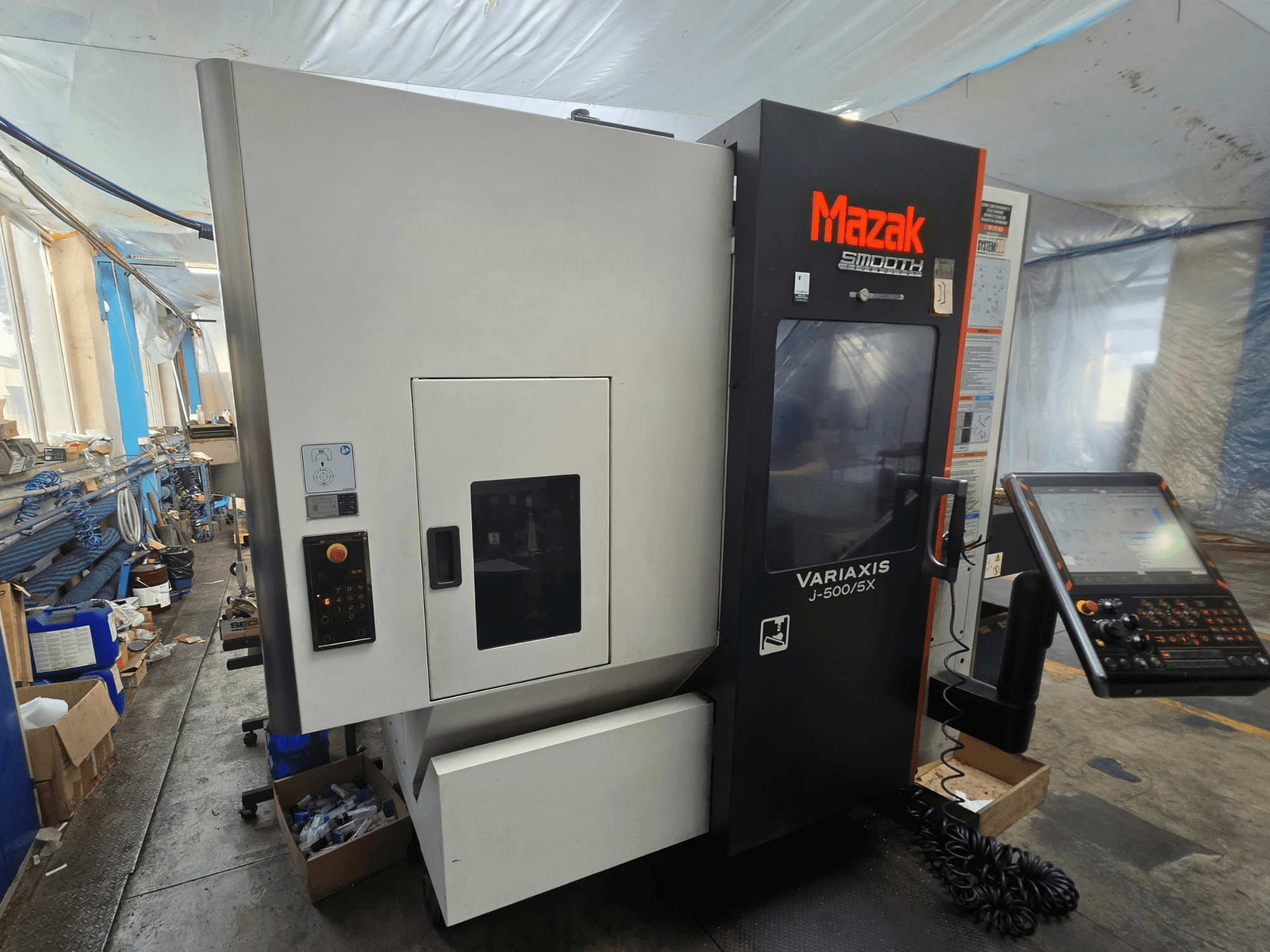 Centro de mecanizado vertical Mazak VARIAXIS J-500/5X, vista lateral en la que se aprecian los mandos y la pantalla, instalado en un taller.