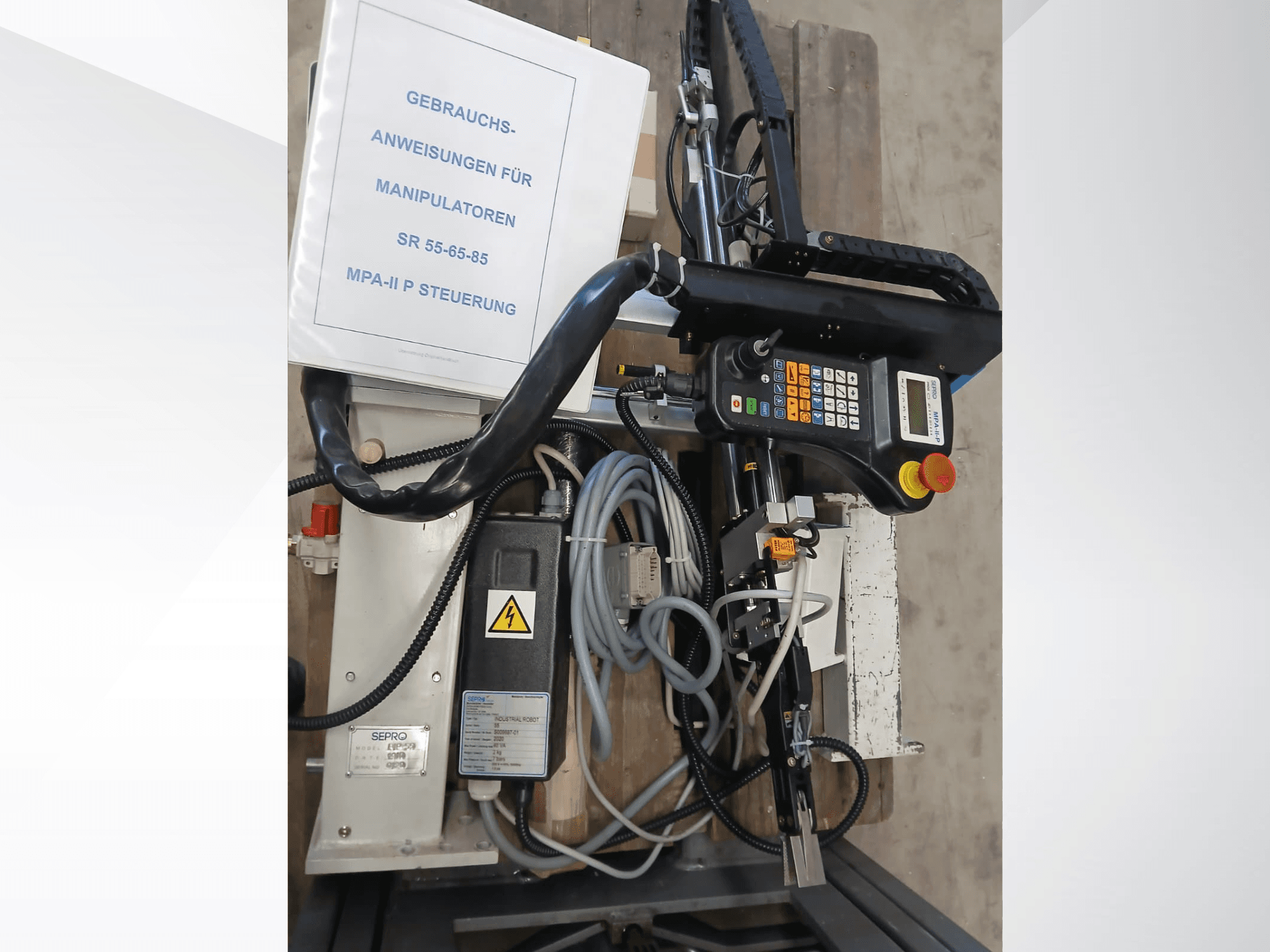 Panel de control y componentes del robot de pórtico Sepro PIP-55, visto lateralmente, con el manual de usuario visible.