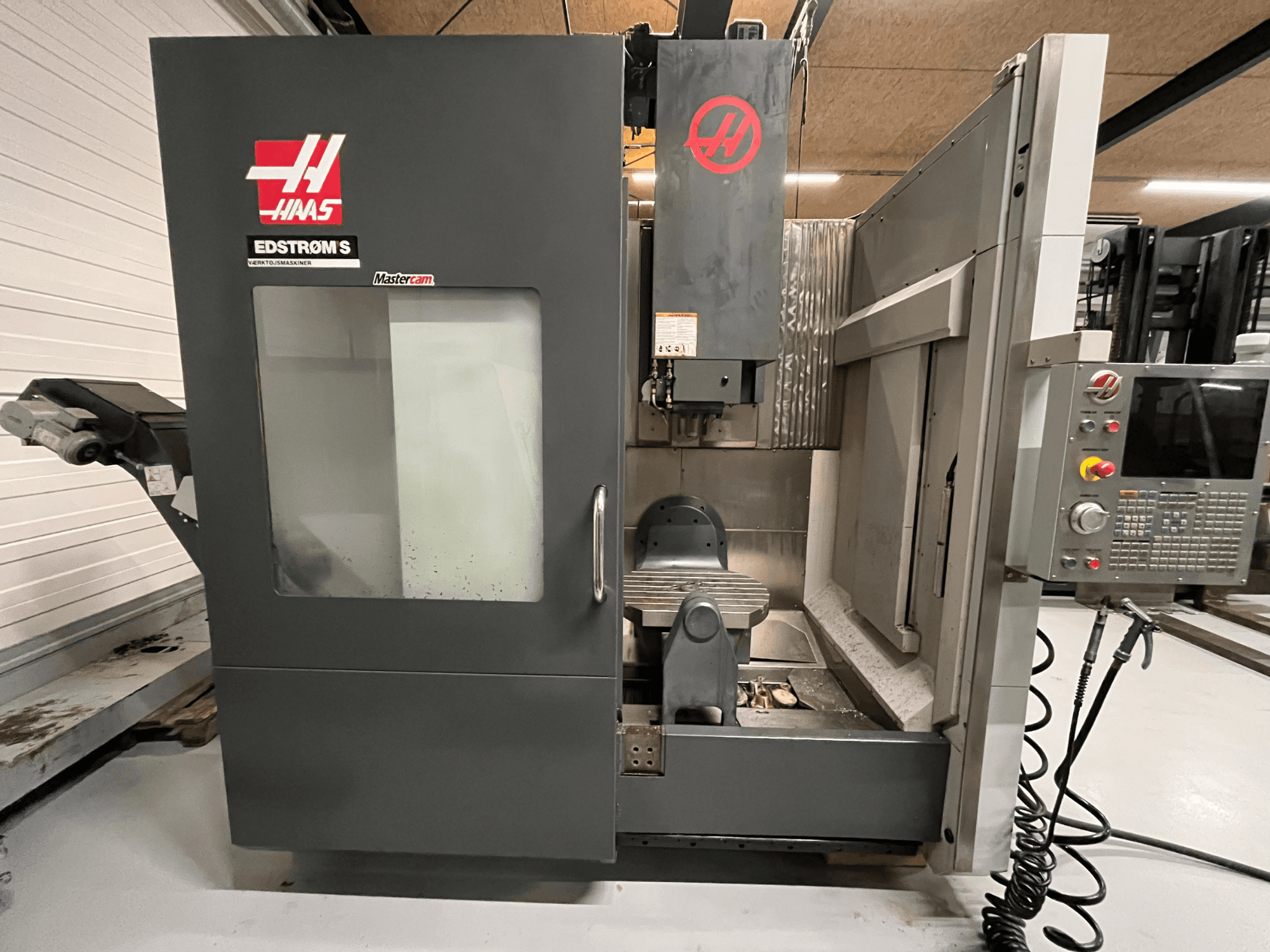 Vista frontal de la máquina CNC EDSTROM S de Haas que muestra el panel de control, el cabezal del husillo y la mesa de mecanizado.