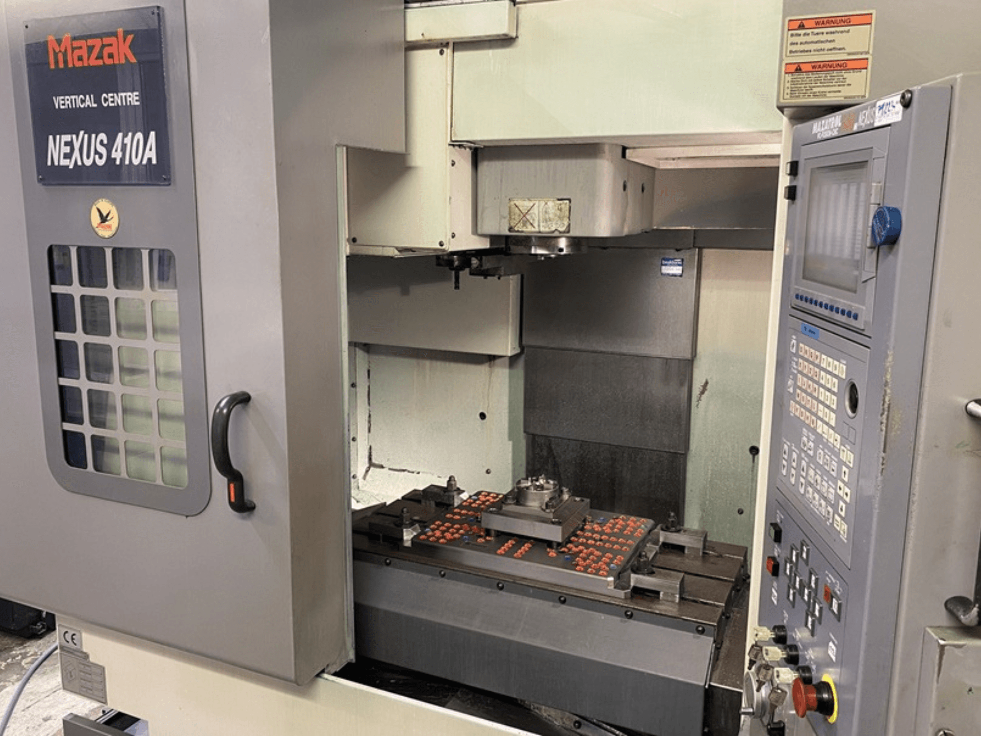 Centro de Mecanizado Vertical Mazak VCN410, vista frontal mostrando el panel de control y el interior de la máquina con la pieza montada.