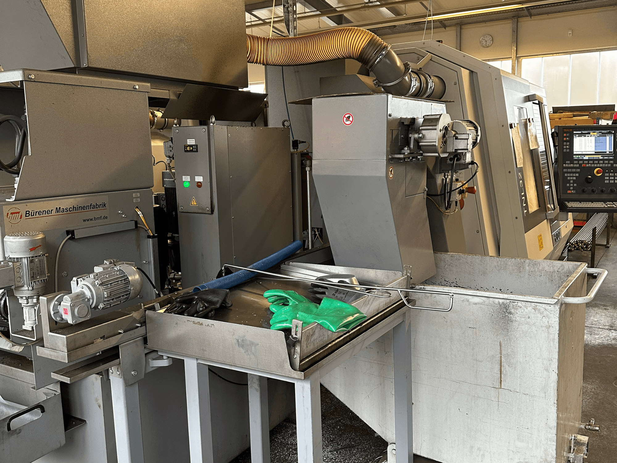 Máquina de torneado tipo suizo TRAUB TNL32-9, vista lateral, mostrando el panel de control, el motor y la zona de corte con virutas de metal.