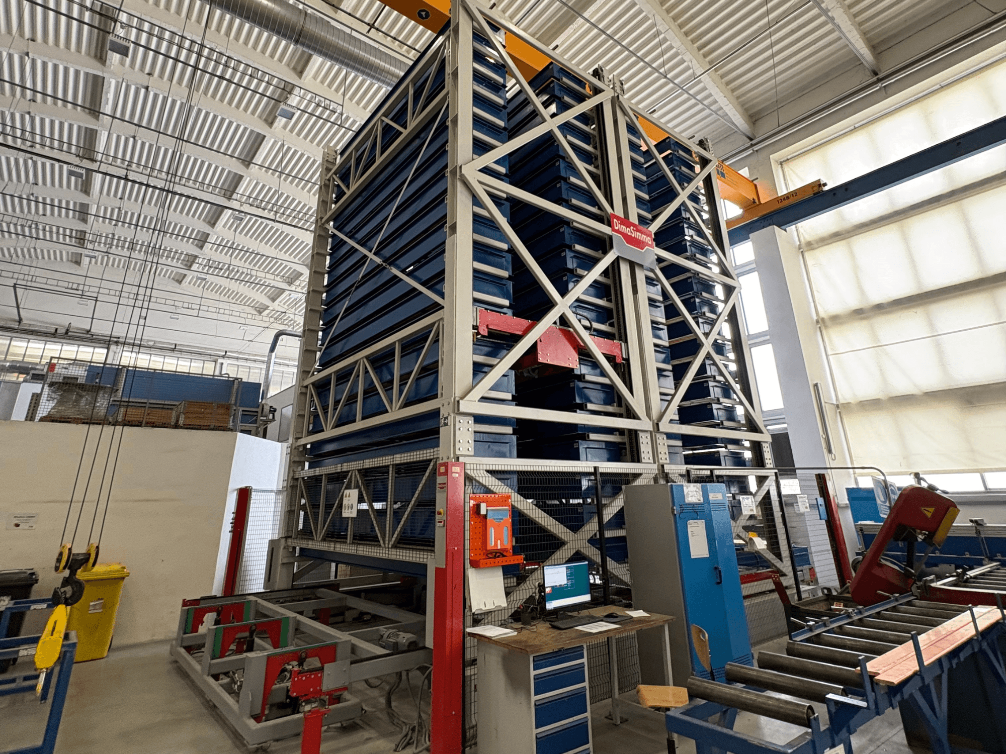 Máquina de chapa DimaSimma EMS-30 TWIN en un taller, vista frontal con bandejas azules apiladas y puesto de control visible.