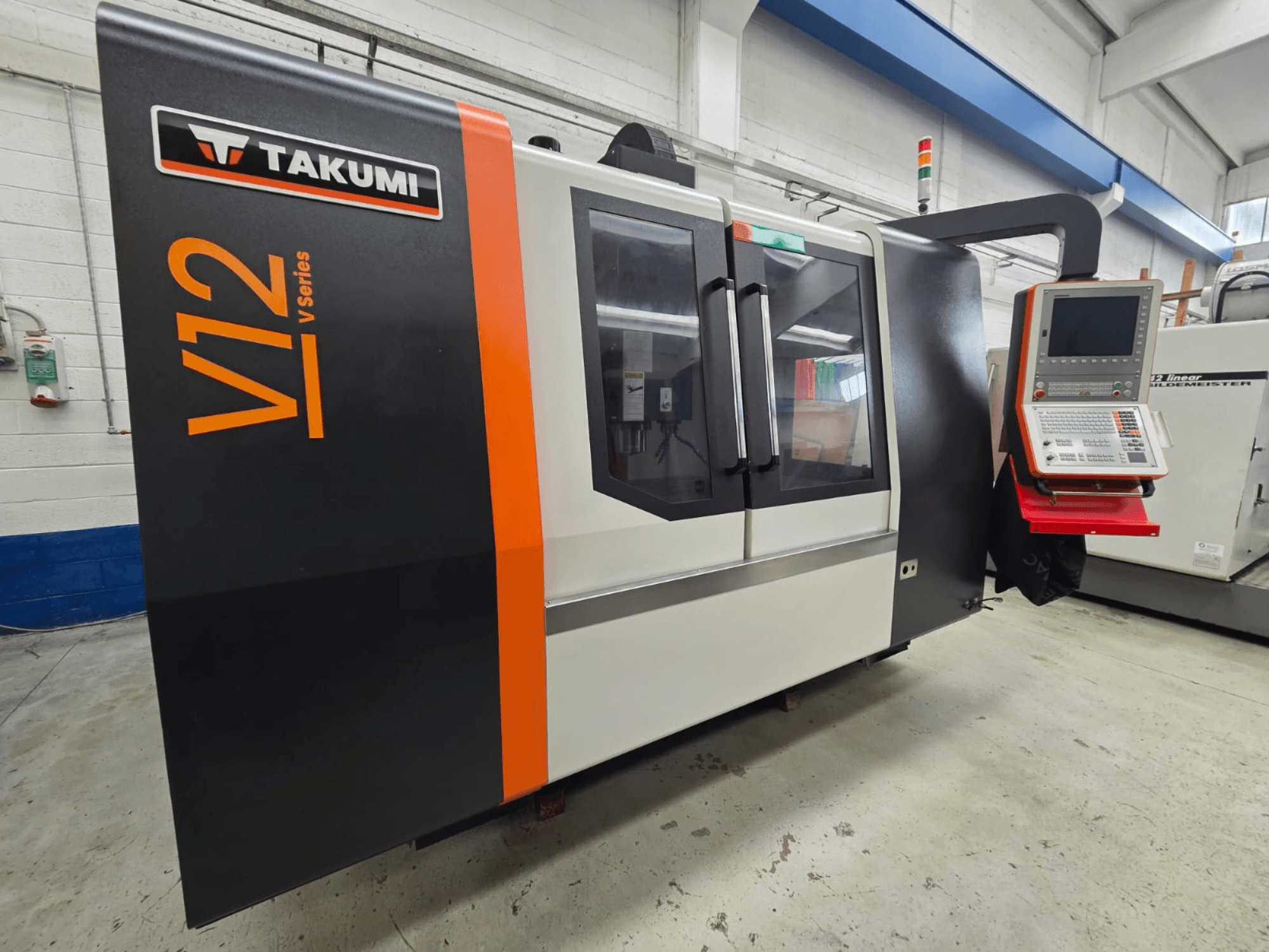 Fresadora CNC Takumi serie V12 V, vista frontal, cuenta con un panel de control y grandes ventanas de cristal.
