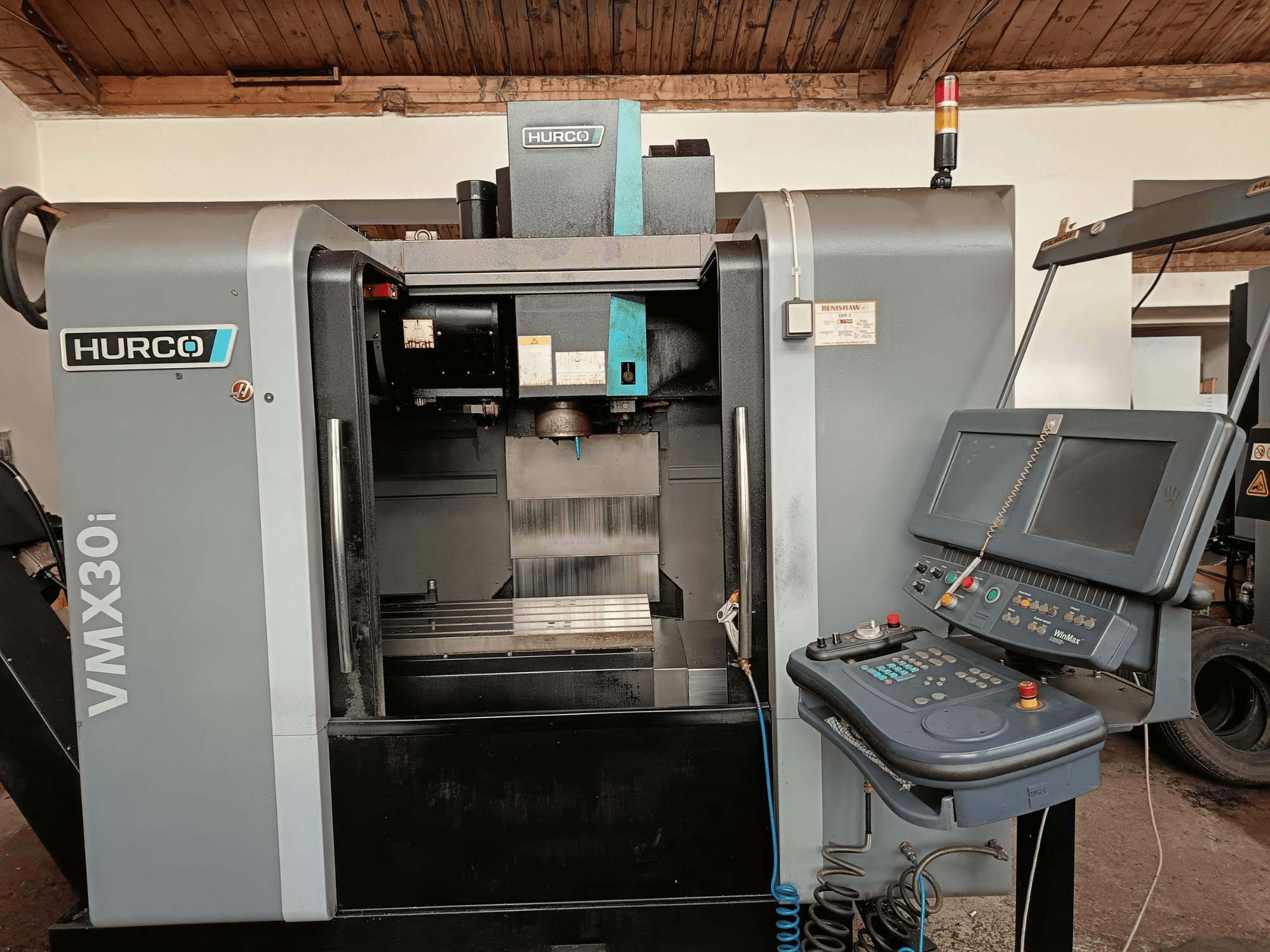 Centro de mecanizado HURCO VMX30i en vista frontal, con panel de control con botones y monitor, área de trabajo metálica y luz de advertencia.