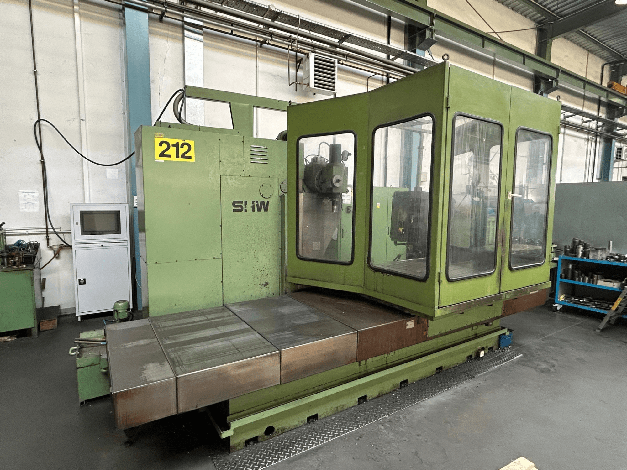 Centro de mecanizado vertical SHW UF-5 en verde, vista frontal que muestra el panel de control, la carcasa de cristal y la mesa de trabajo metálica.