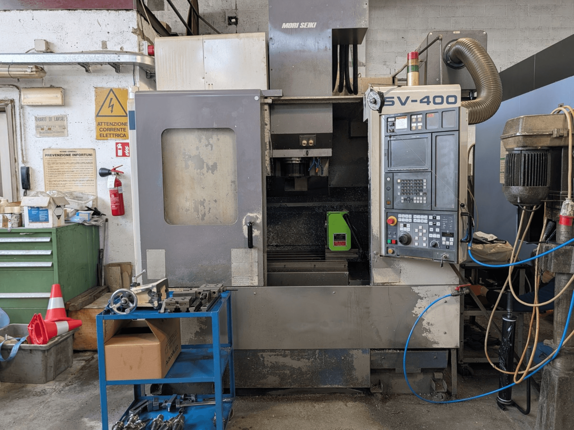 Centro de mecanizado vertical MORI SEIKI SV-400 en un taller, vista lateral, mostrando el panel de control y las máquinas herramienta cercanas.