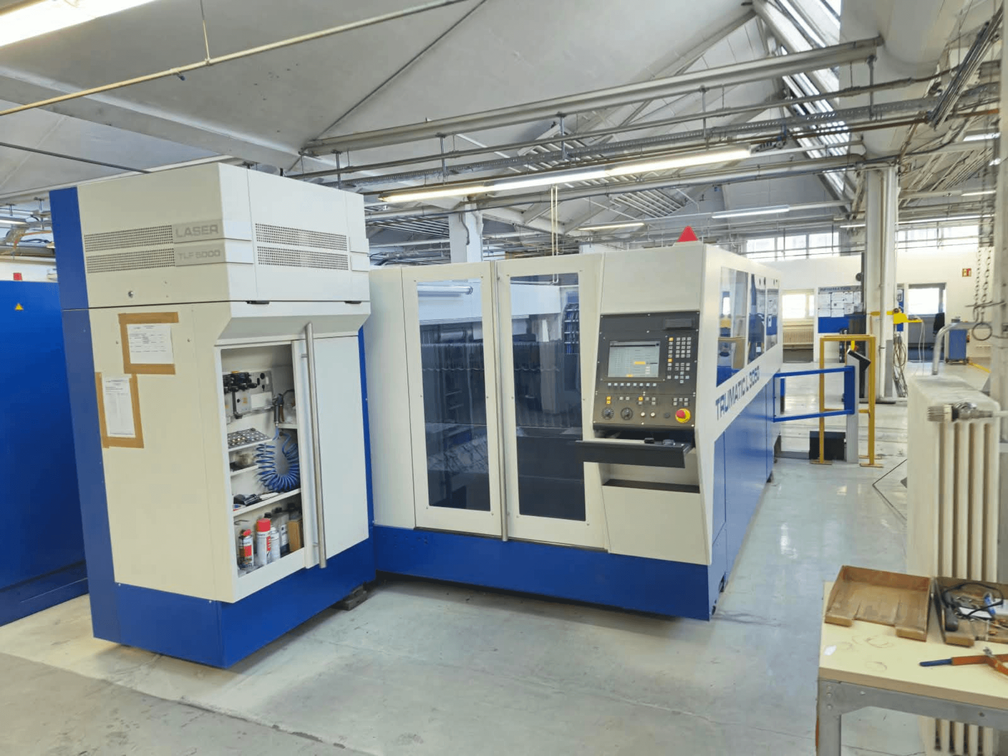 Máquina de corte por láser de CO₂ TRUMPF TruLaser L3050, vista frontal, con el panel de control y la puerta de acceso para el mantenimiento, en su configuración de fábrica.