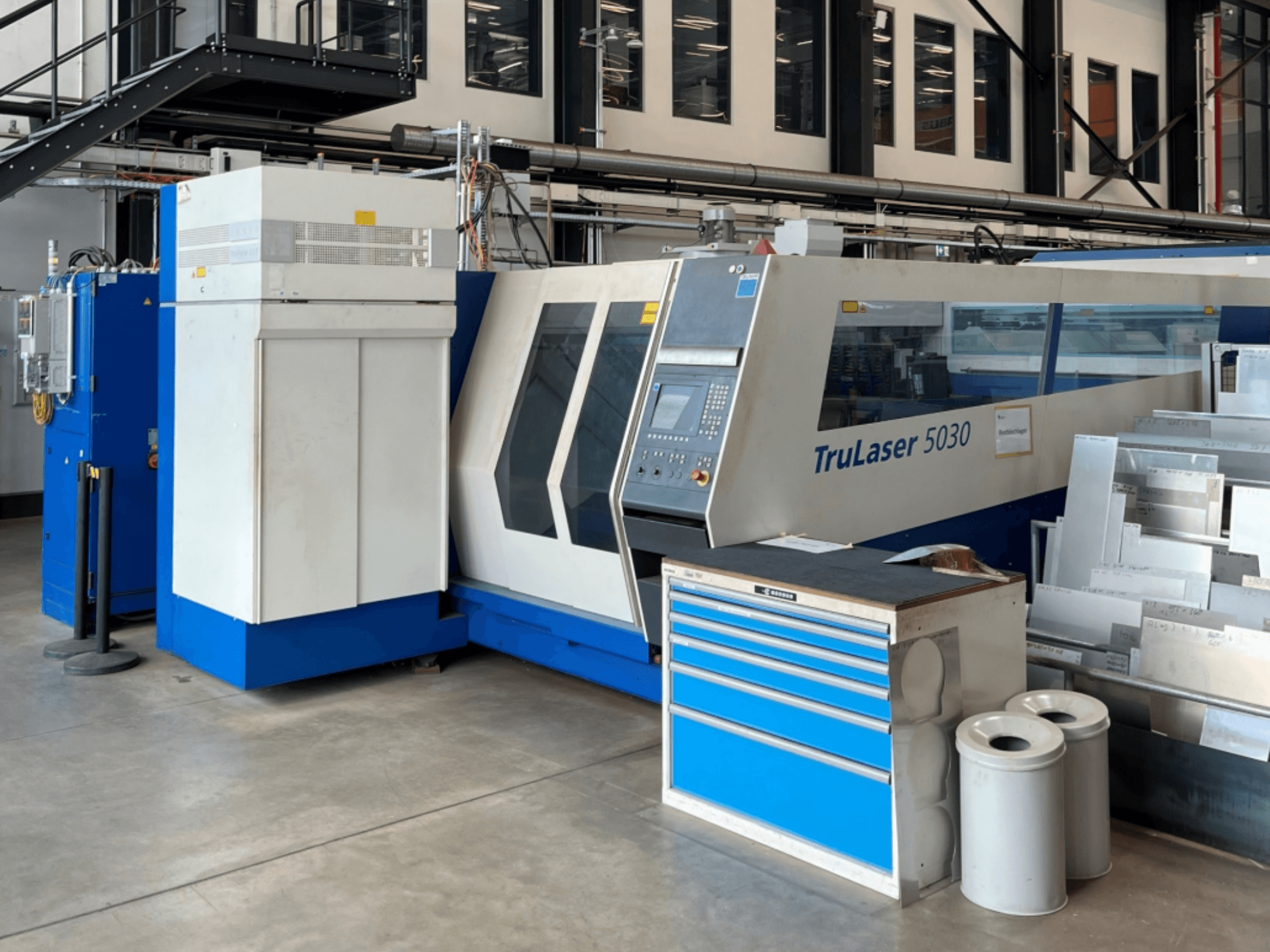 Máquina de corte por láser de CO₂ TRUMPF TruLaser 5030 vista de frente, en la que se aprecian el panel de control y la mesa de trabajo situada junto a ella con chapas metálicas.