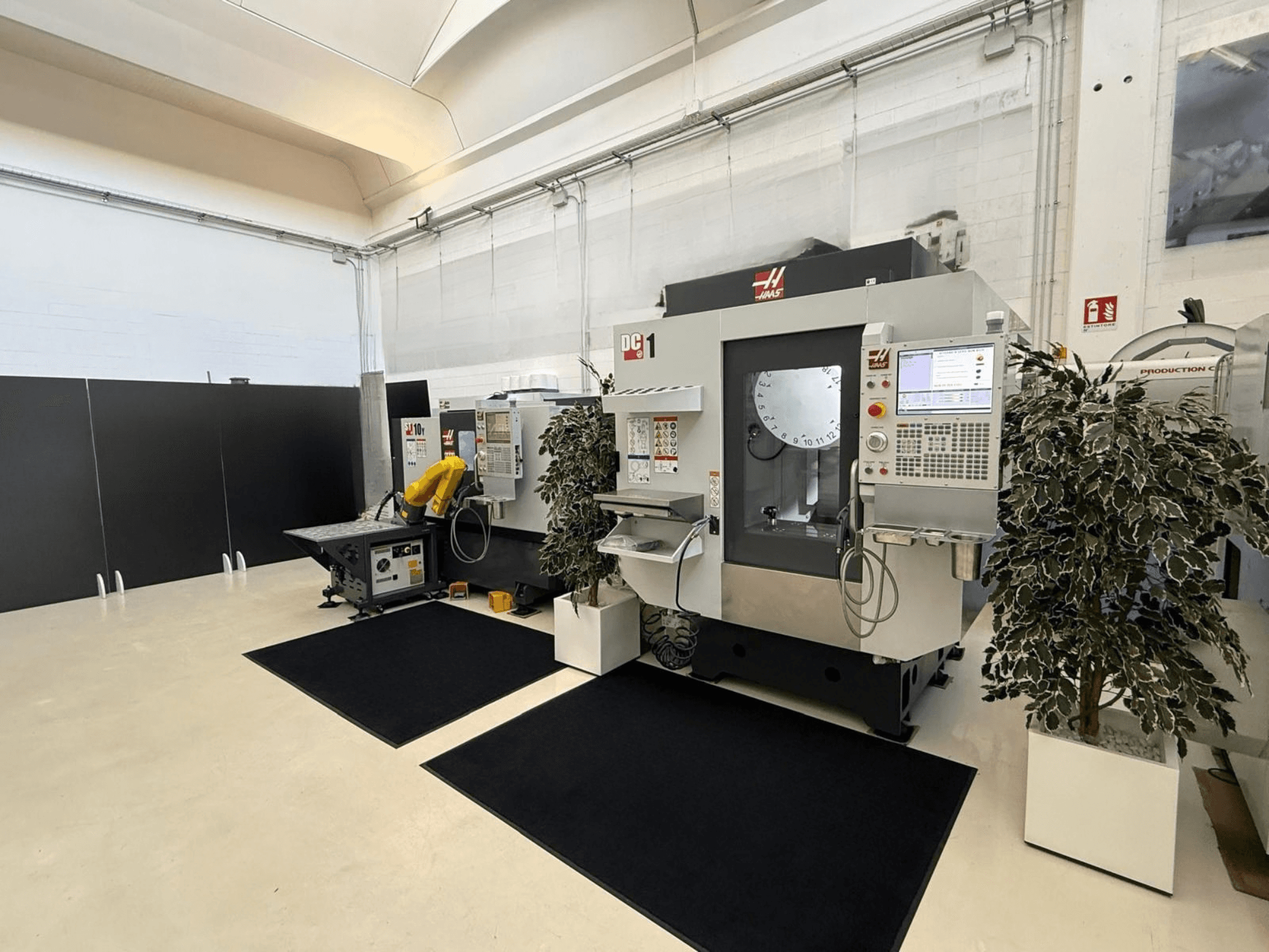 Vista frontal de un centro de mecanizado vertical HAAS DC-1 en un espacio de trabajo limpio, con un panel de control con pantalla táctil y las instalaciones circundantes.