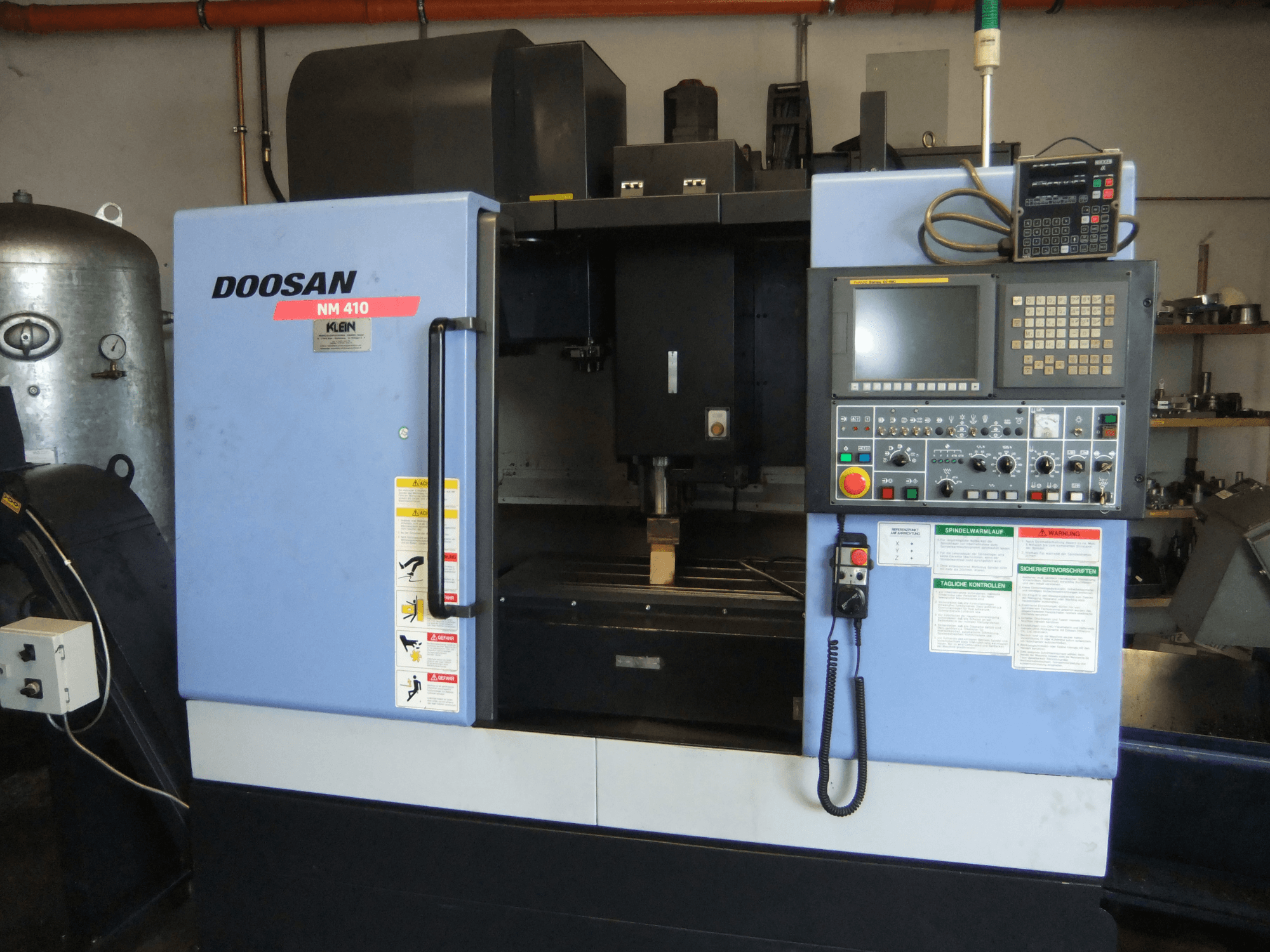 Centro de mecanizado vertical DOOSAN NM 410, vista frontal, en la que se aprecian el panel de control, la zona del husillo y las etiquetas de seguridad.