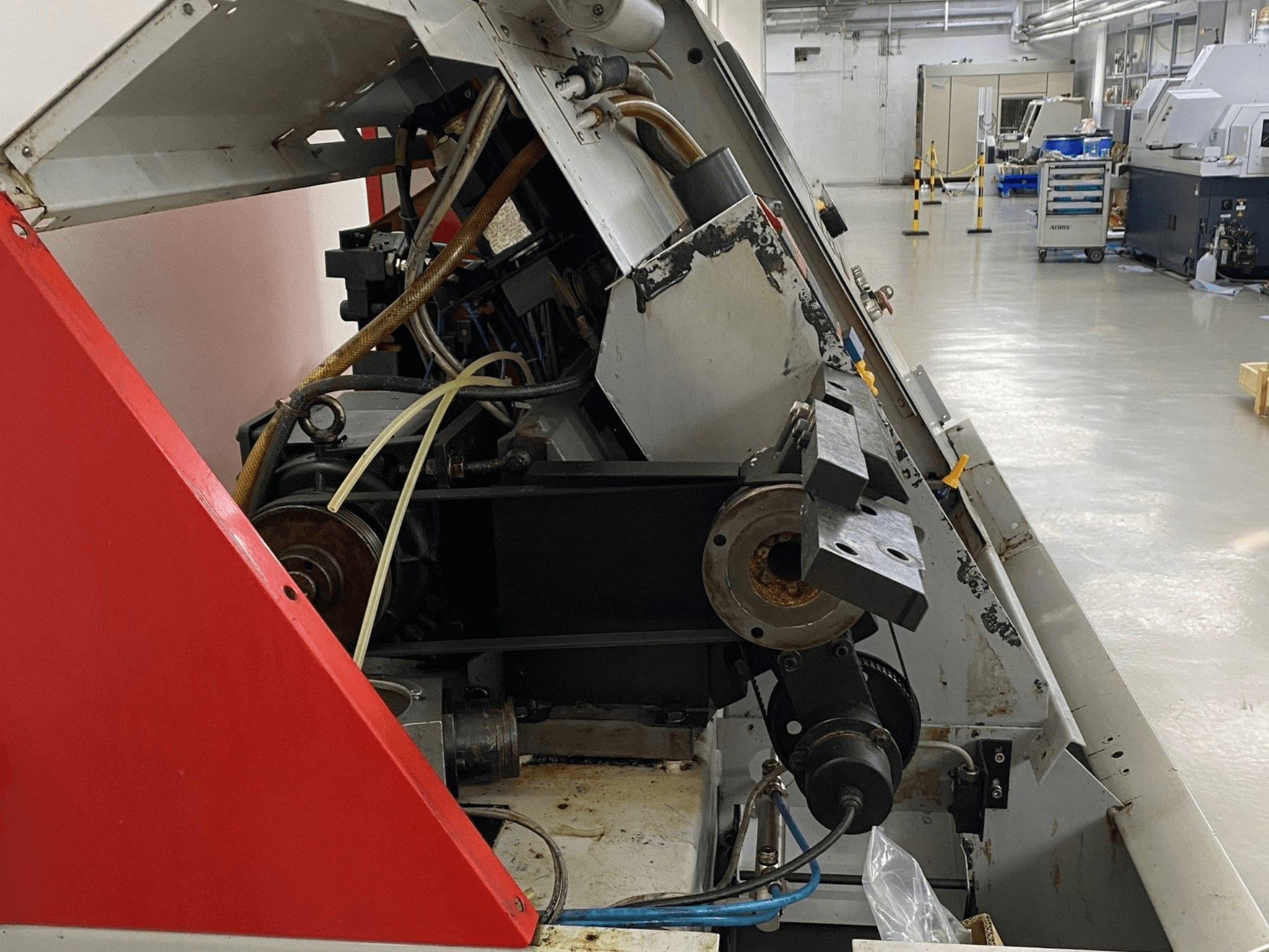 Máquina de torneado horizontal EMCO Emcoturn 325, vista lateral que muestra los componentes de accionamiento y el sistema hidráulico en un entorno industrial.