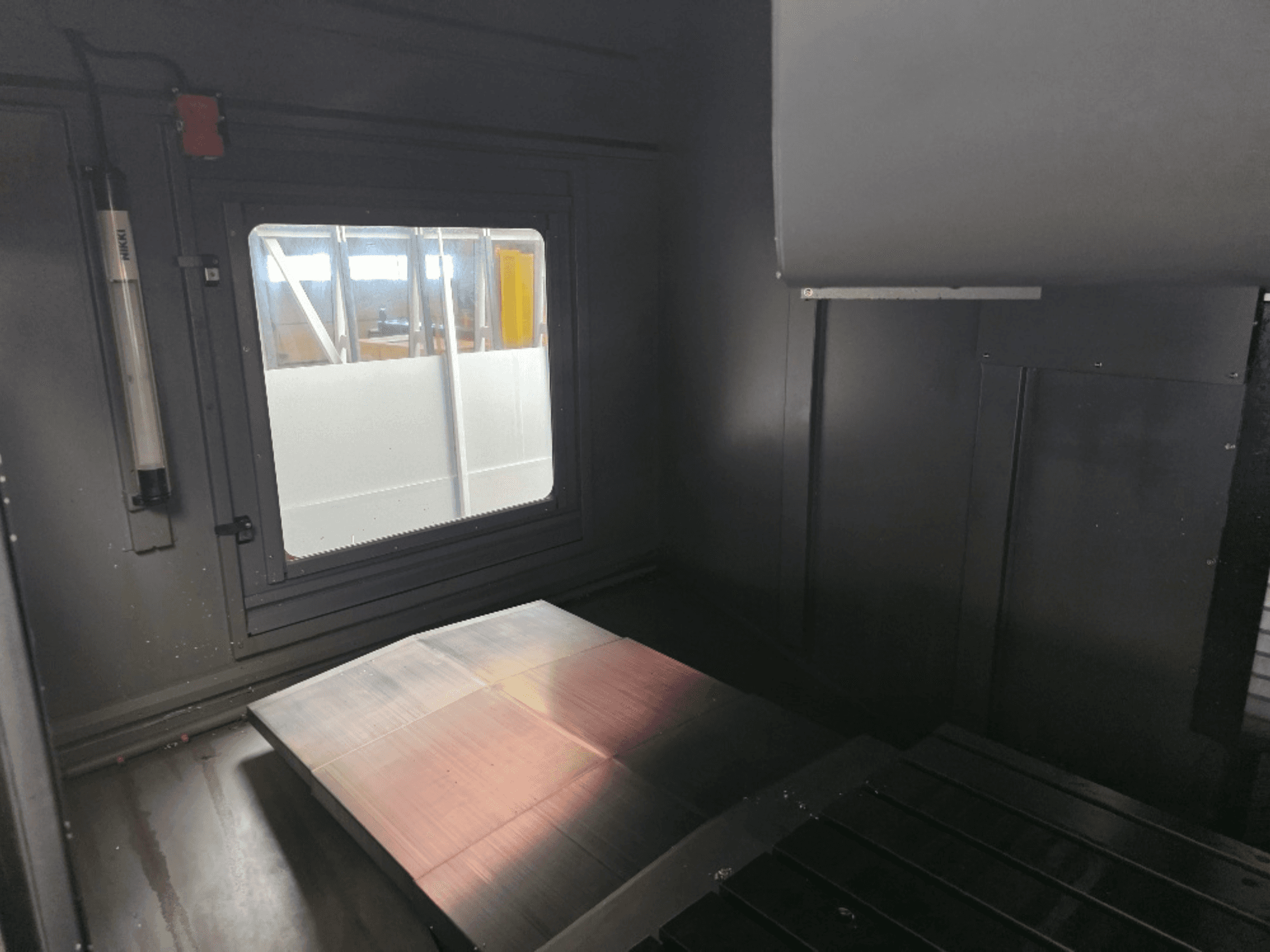 Vista interior de una caja de máquina con una placa de metal pulido, una ventana lateral y una iluminación mínima. No se ve ninguna marca.