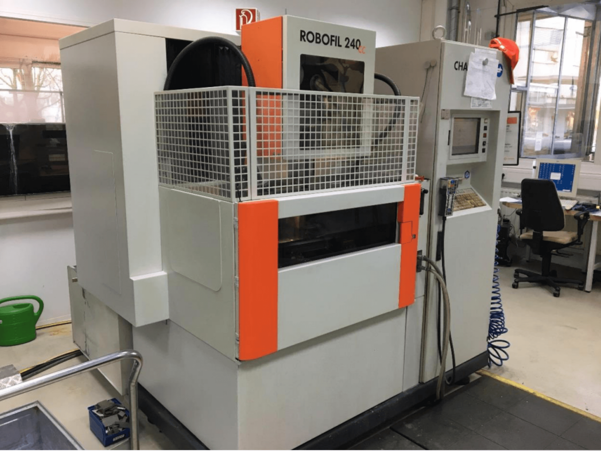 Vista frontal de la máquina de electroerosión por hilo CHARMILLES ROBOFIL 240 CC, que cuenta con una rejilla protectora y un panel de control, situada en un taller.