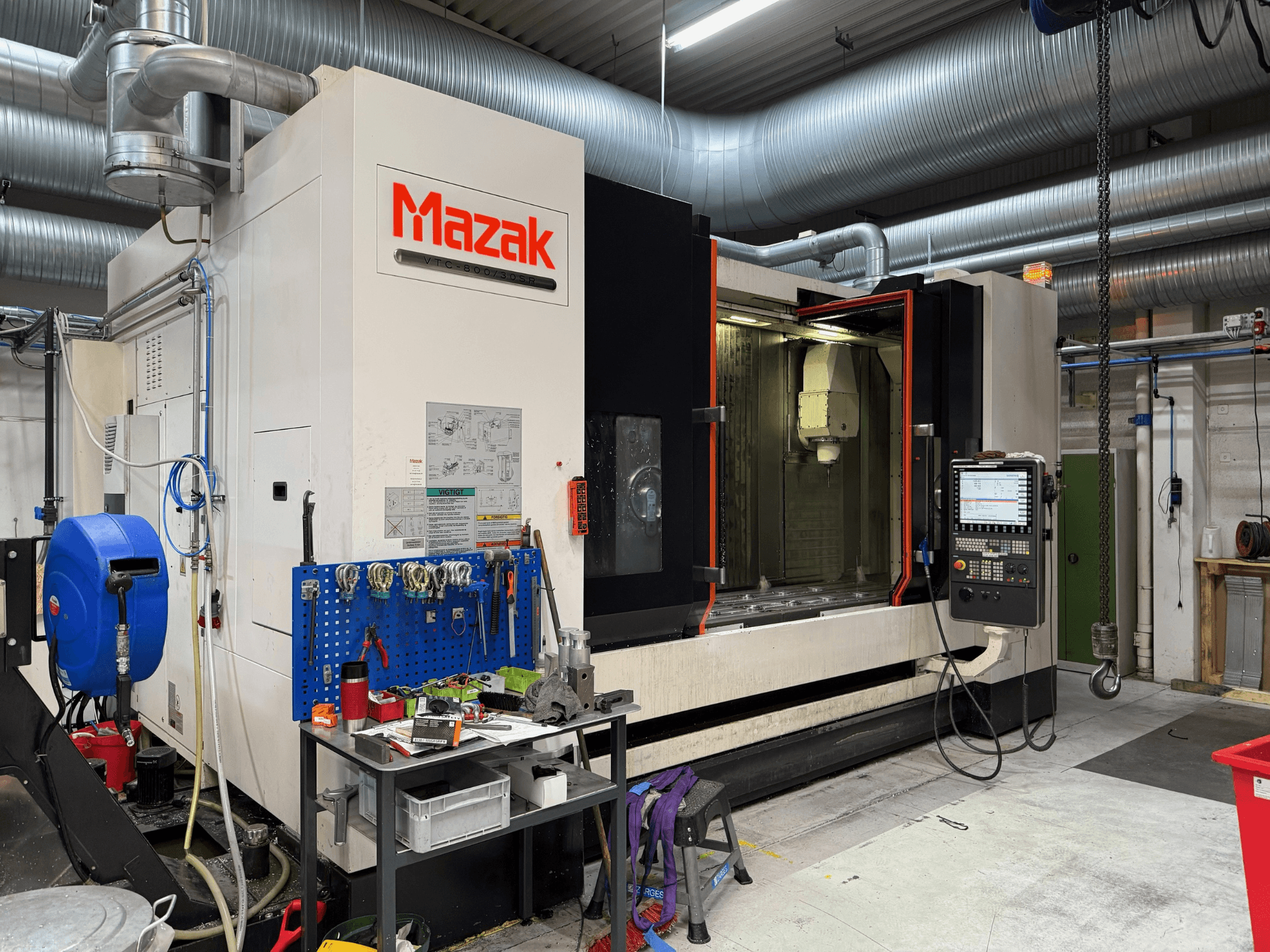 Máquina CNC Mazak desde una vista frontal, con controles, herramientas y espacio de trabajo en un entorno de mecanizado.