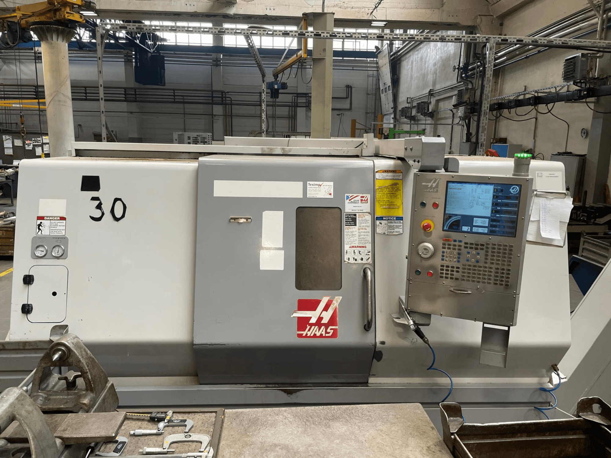 Vista frontal del torno horizontal Haas SL-30THE, en la que se aprecian el panel de control digital, las etiquetas de peligro y el número de modelo 30.
