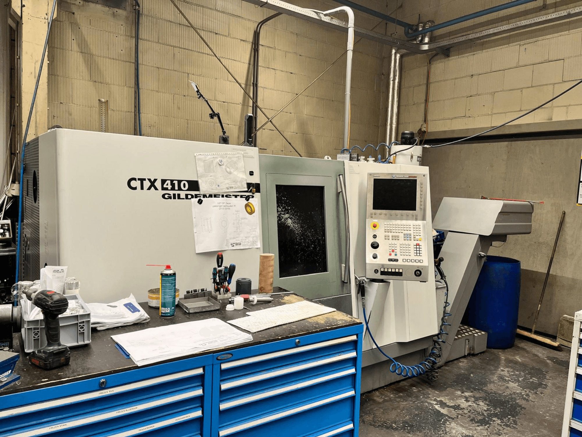 Máquina CNC Gildemeister CTX 410 en un taller, vista frontal, con un panel de control y varias herramientas sobre un banco de trabajo.