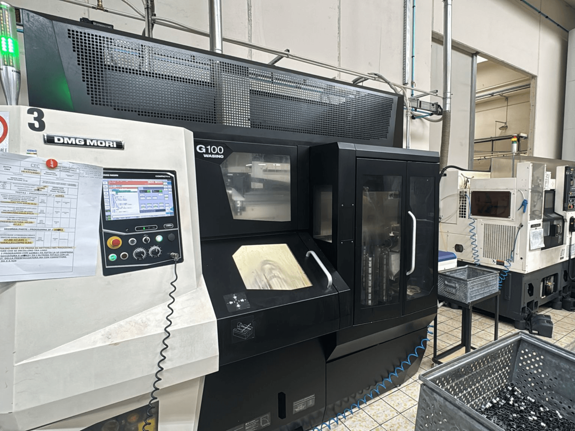 Máquina DMG MORI G100 en una fábrica, vista frontal, con un panel de control digital y depósitos de herramientas cercanos.