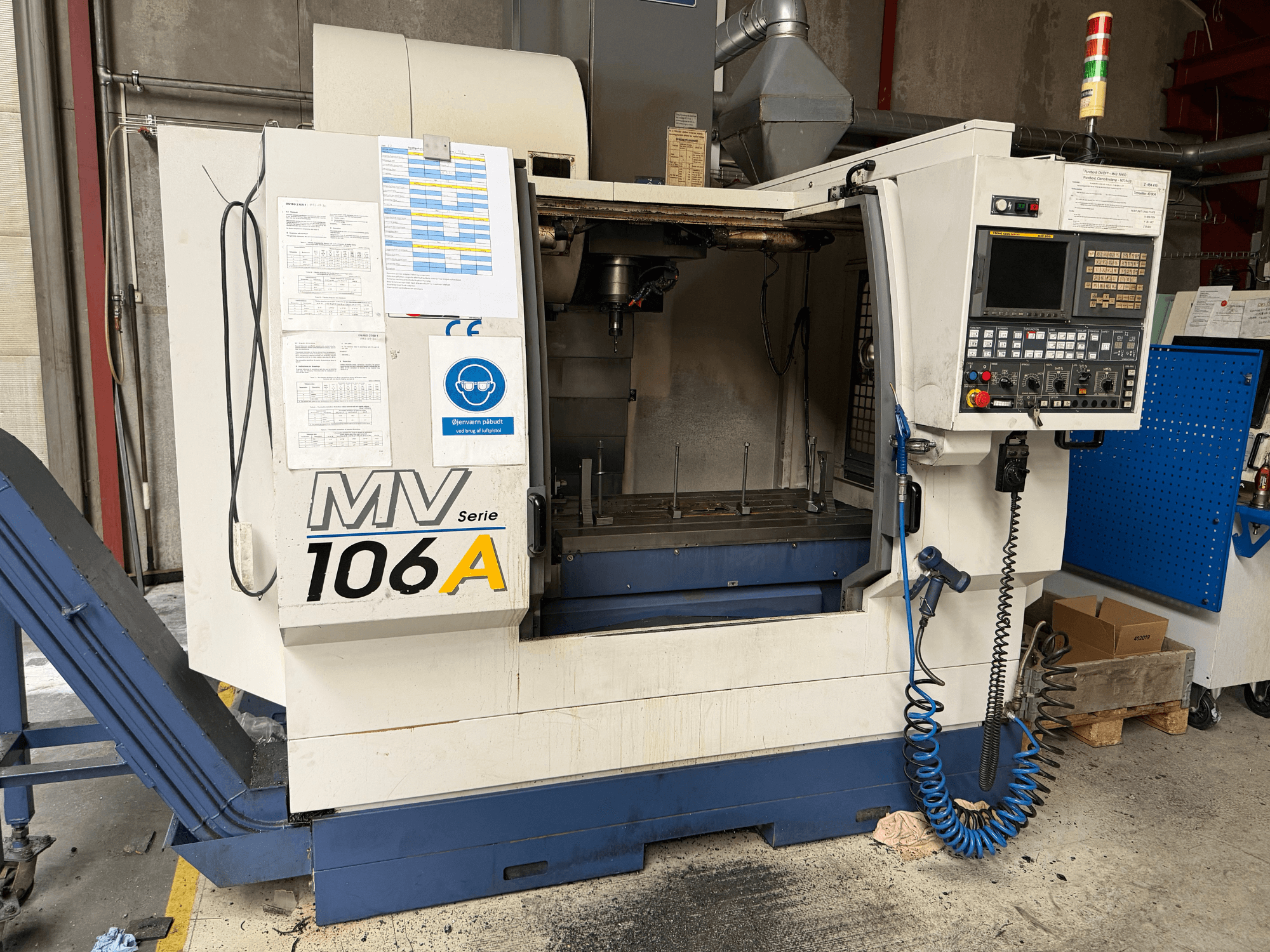Centro de mecanizado vertical YCM MV106A, vista frontal en la que se aprecian el panel de control y el espacio de trabajo, con la documentación técnica adjunta.