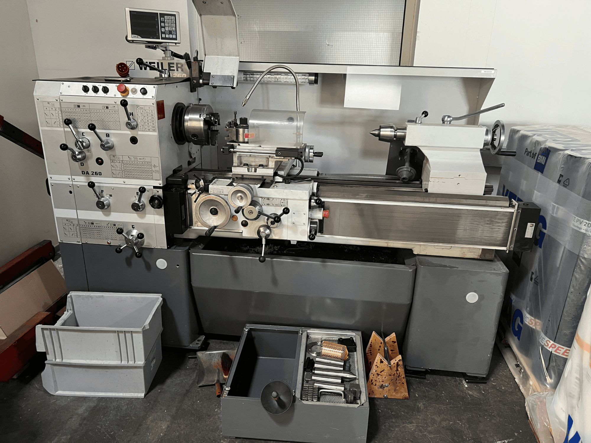 Torno horizontal Weiler DA 260 X 1000 visto de frente, con el panel de control y las herramientas, y con compartimentos de almacenamiento en la parte inferior.