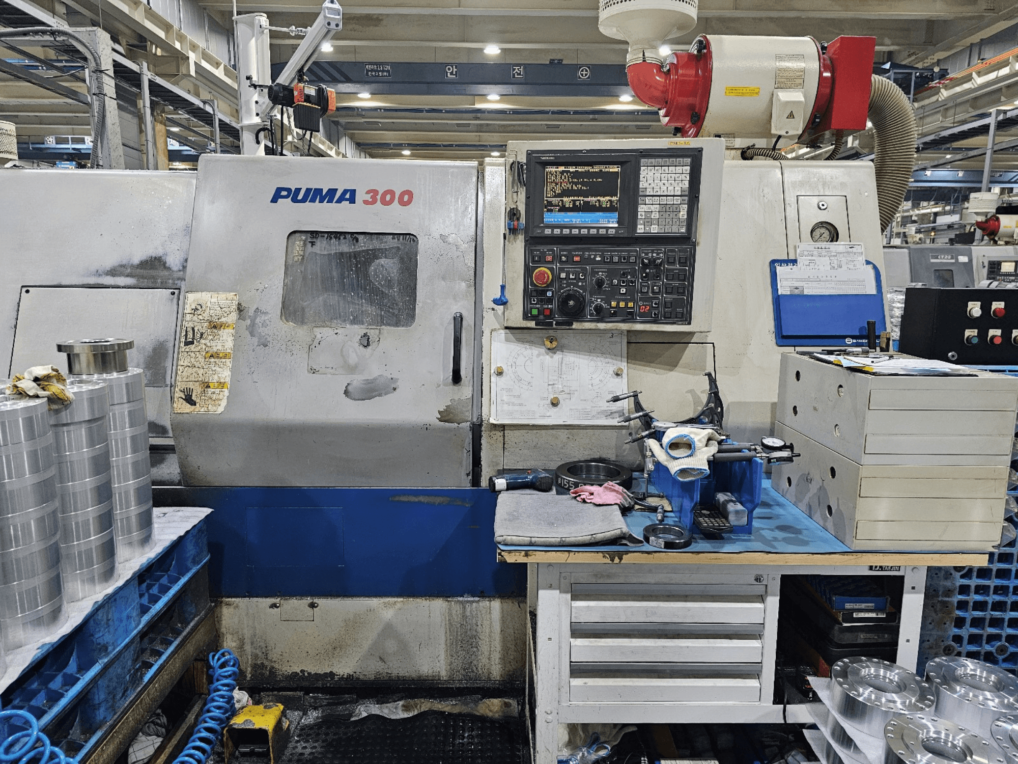 Máquina CNC PUMA 300 en un taller; vista frontal que muestra el panel de control, las herramientas y las piezas metálicas en un banco de trabajo.