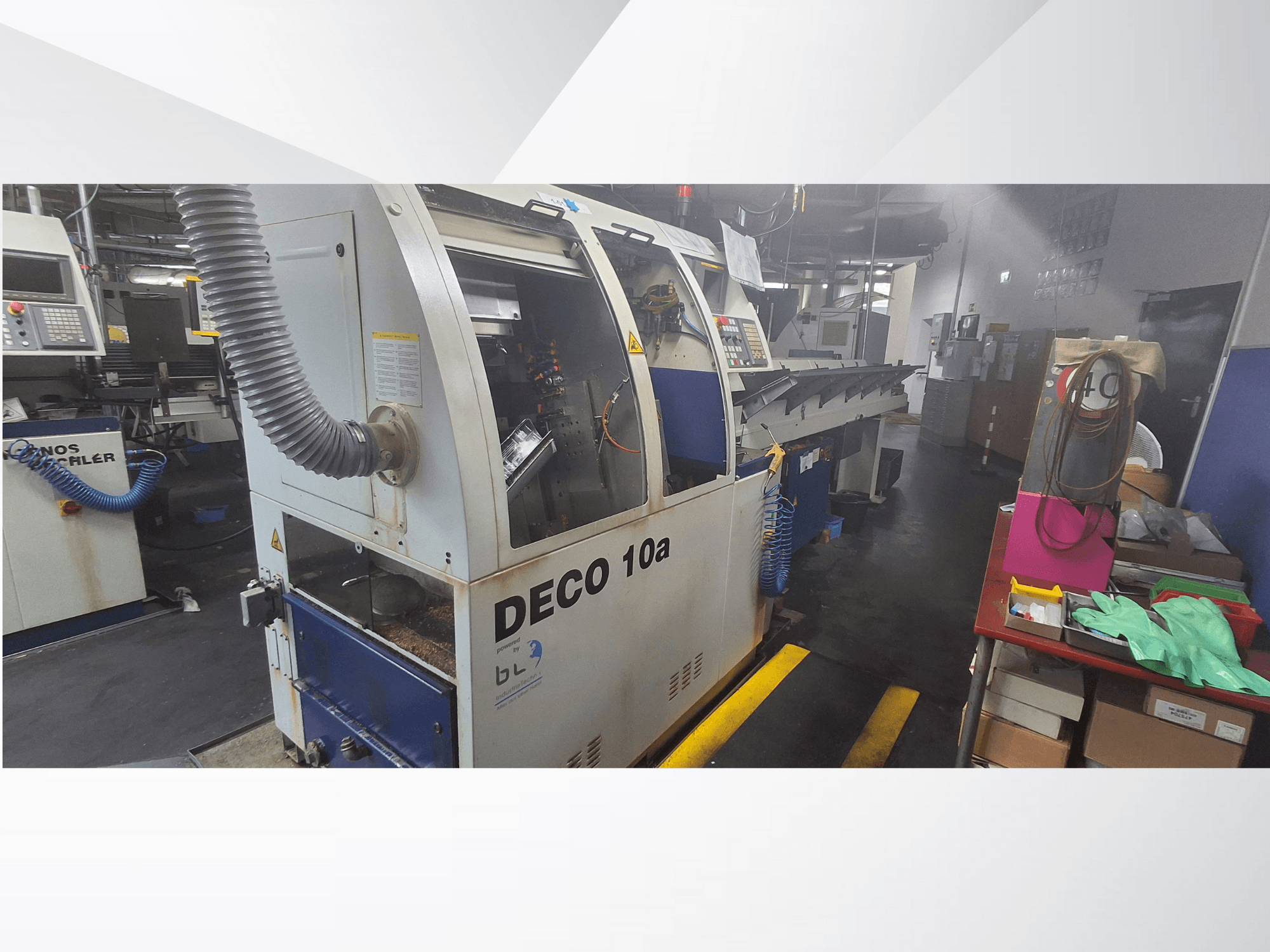 Máquina CNC DECO 10a en un taller, vista frontal; cuenta con un panel de control y un sistema de extracción de polvo, con un banco de trabajo cerca.