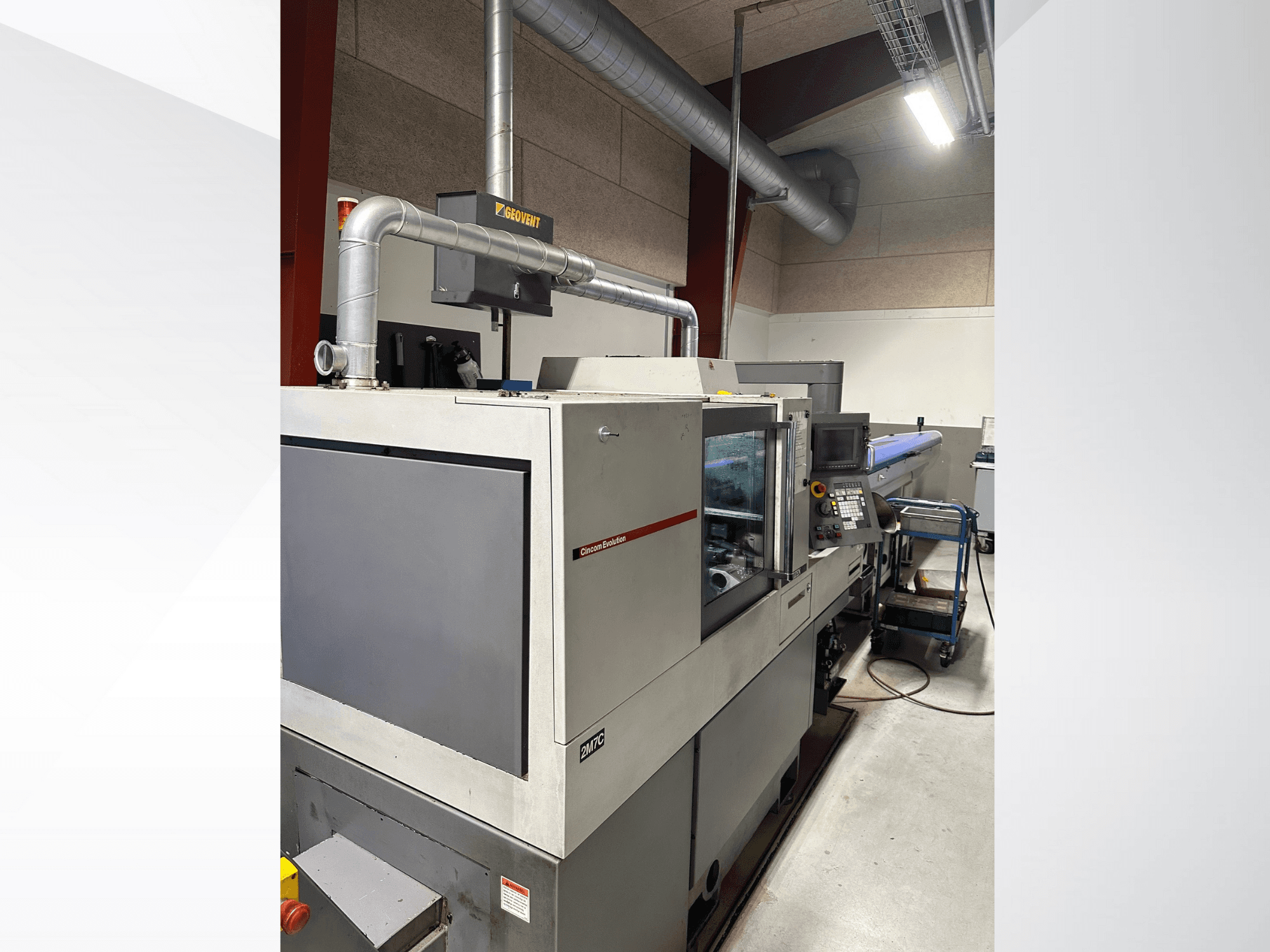 Maquinaria industrial de la marca MVC, vista lateral con panel de control y conductos visibles, ambientada en una fábrica.