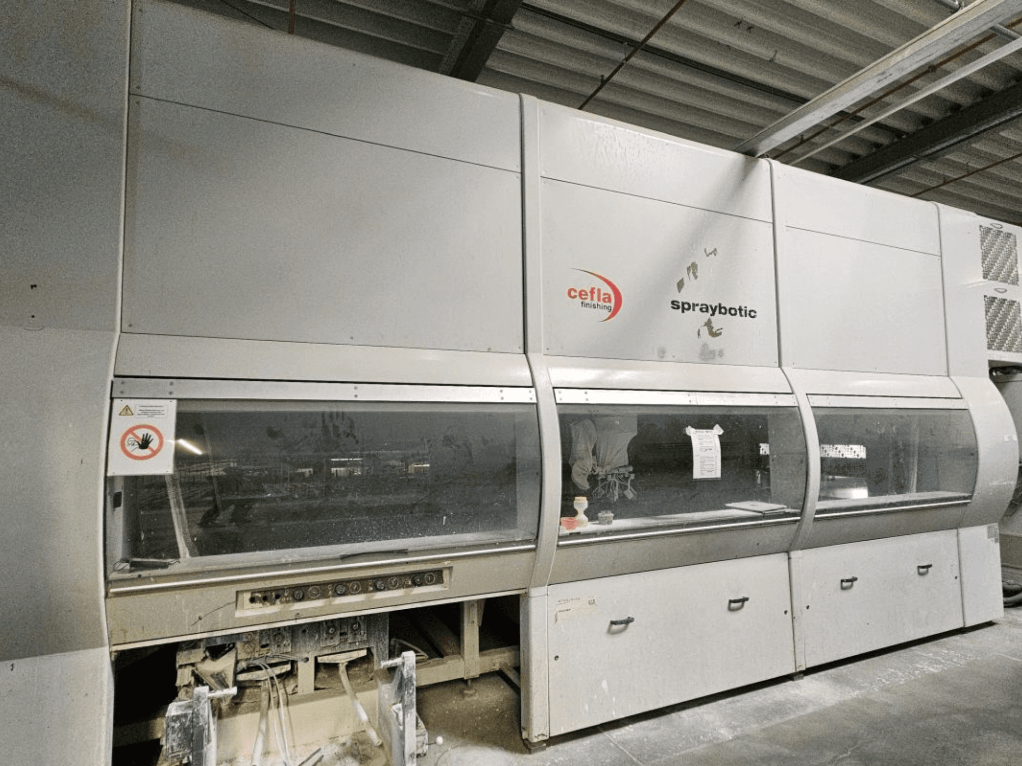 Línea de producción Cefla Spraybotic MD para madera, vista frontal, mostrando el panel de control y las ventanas de visualización transparentes.
