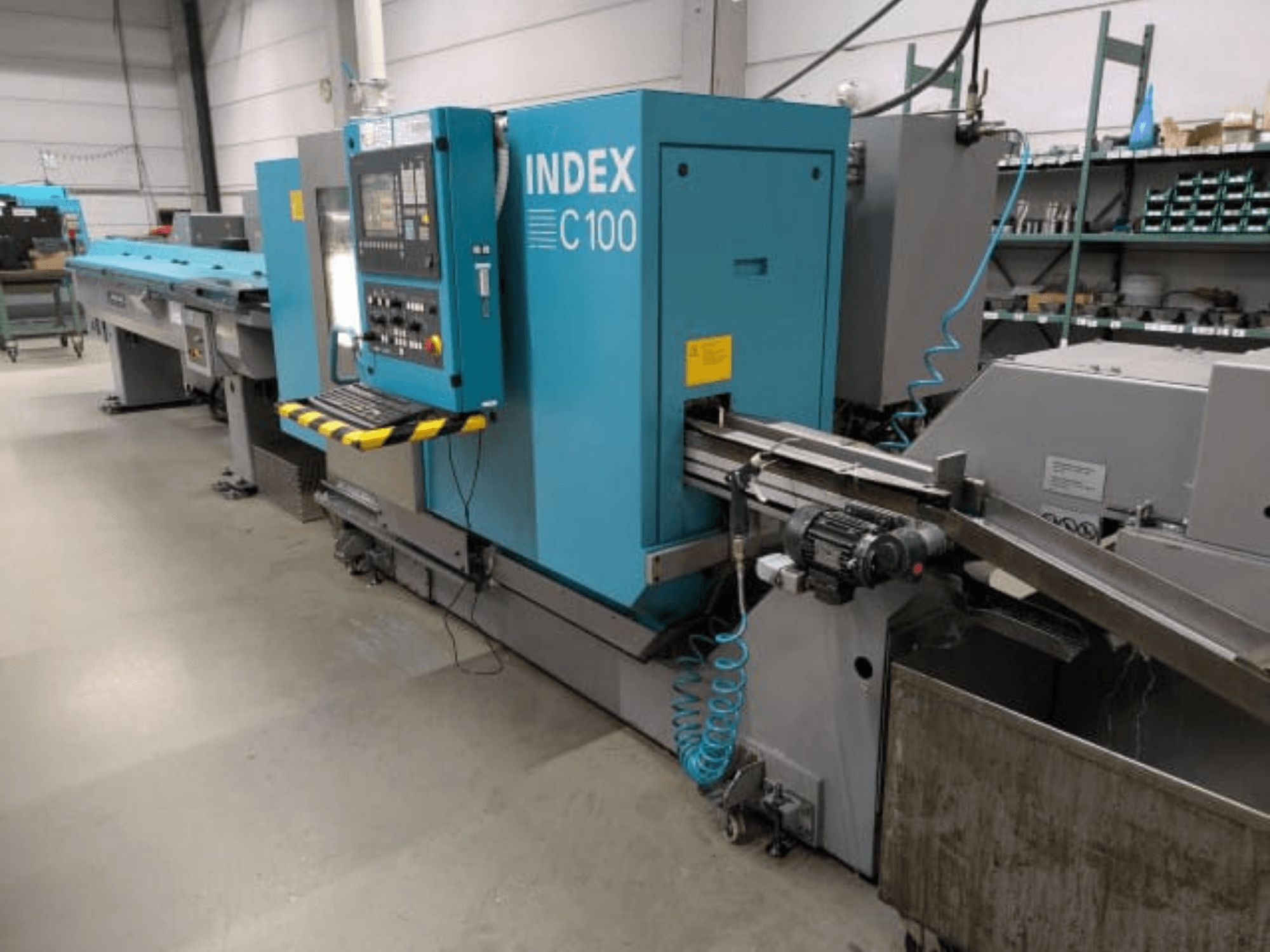 Máquina de torneado horizontal Index C100, vista lateral; cuenta con un panel de control, un sistema de avance y un contenedor para la recogida de virutas metálicas.