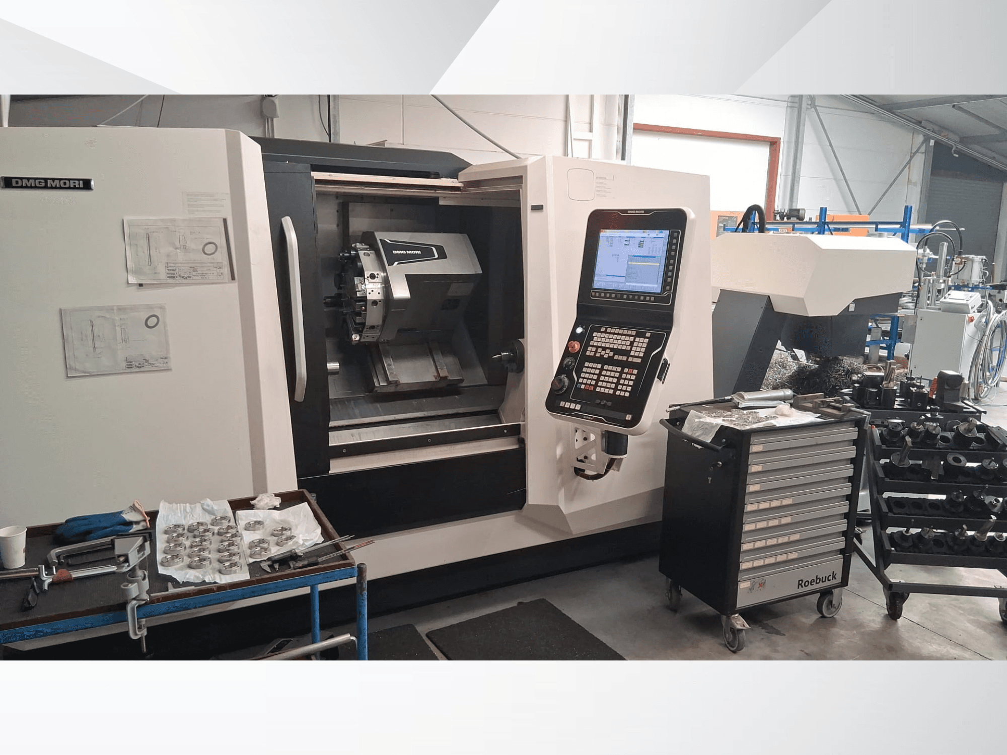 Máquina de torneado horizontal DMG MORI CLX450 desde una vista frontal, con panel de control, área de trabajo, herramientas y piezas metálicas.