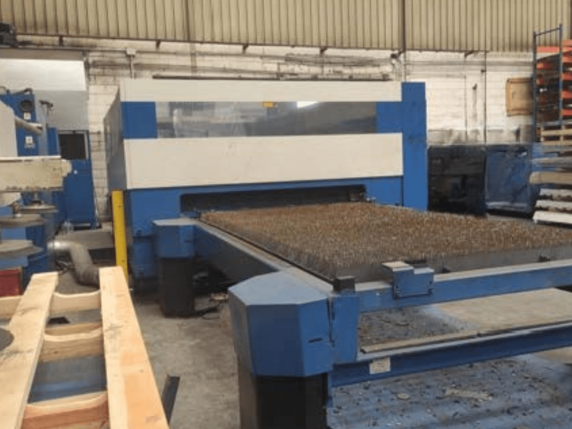 Máquina de corte por láser azul con bancada metálica texturizada, vista lateral, que muestra la configuración operativa en un espacio de trabajo industrial.