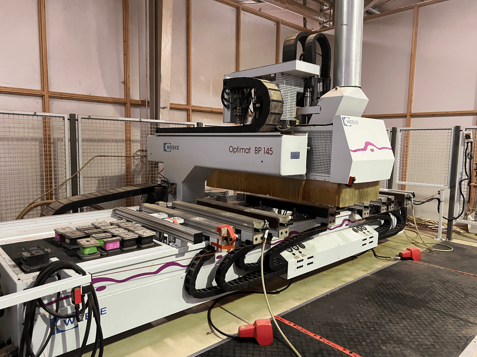 WEEKE Optimat BP 145 en una fábrica, mostrando una máquina CNC con botones de control y cables, vista desde el lateral.