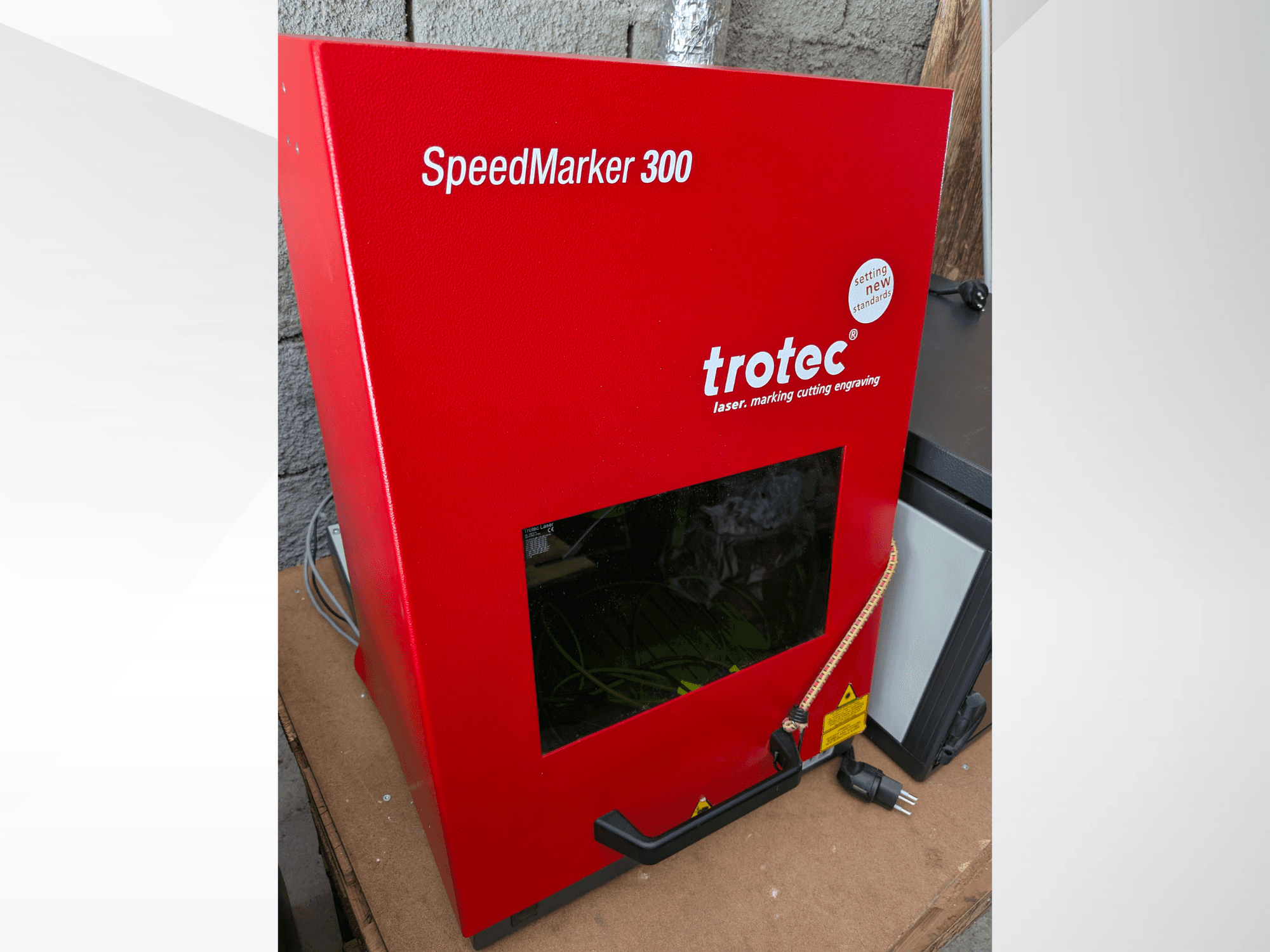 Máquina de marcado láser Trotec SpeedMarker 300 roja en vista frontal, con una gran ventana de visualización y conexión de alimentación.