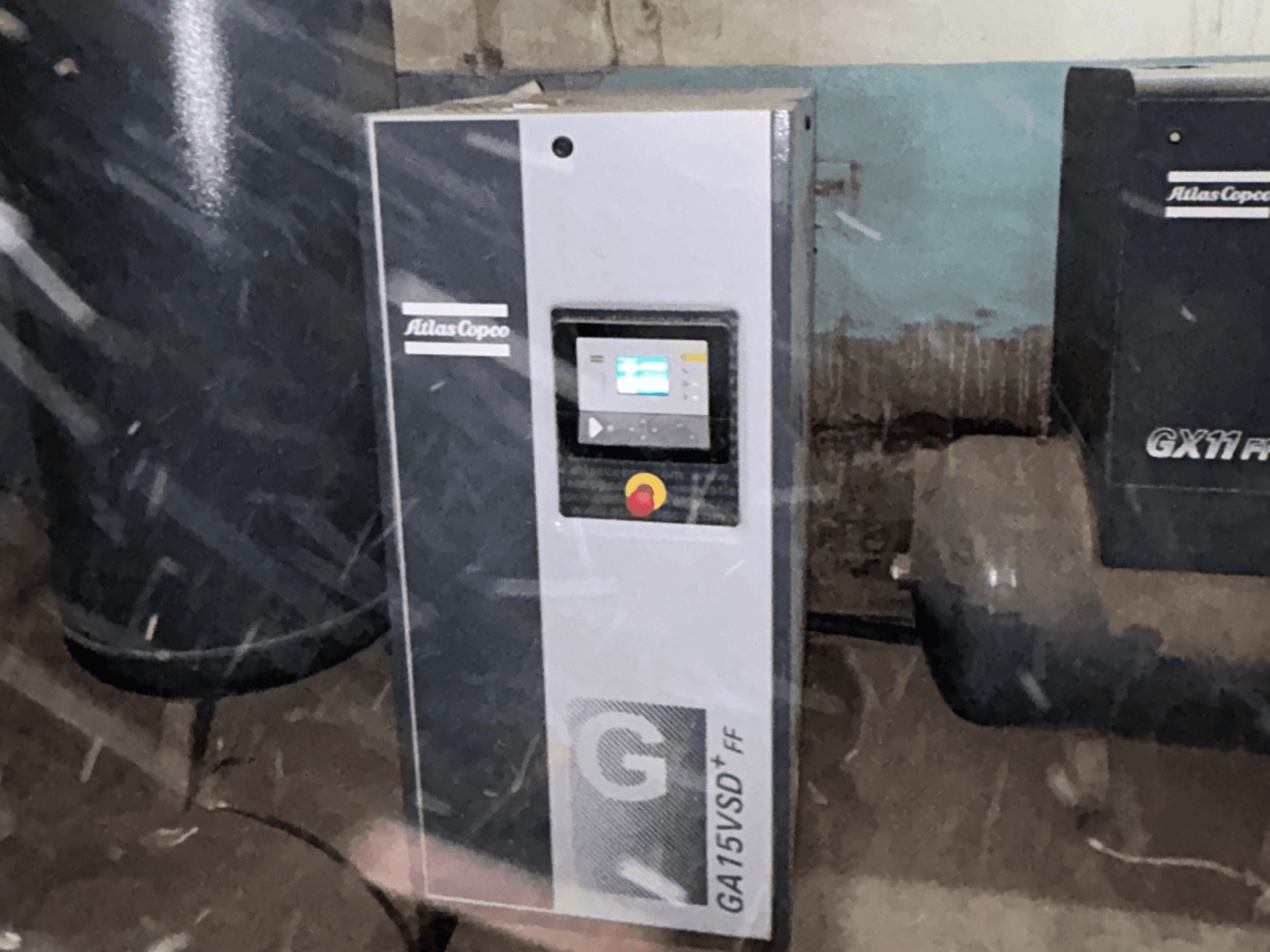 Compresor de aire Atlas Copco GA15VSD+FF, vista frontal, que incluye un panel de control con pantalla y un botón rojo de parada de emergencia.