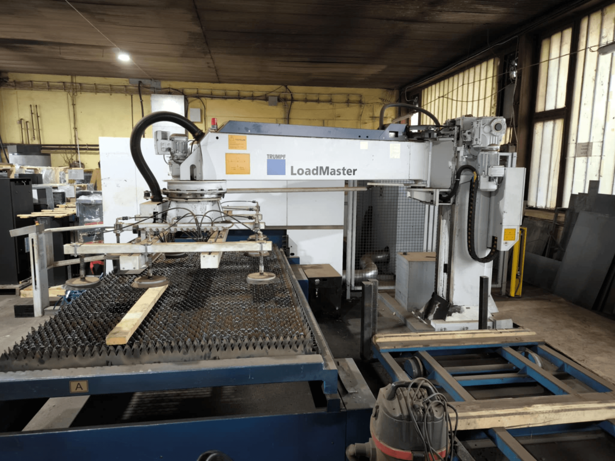 Máquina de corte TRUMPF TRULASER 3030 FIBER, vista frontal, mostrando el sistema LoadMaster y posicionada sobre una mesa de trabajo enrejada.