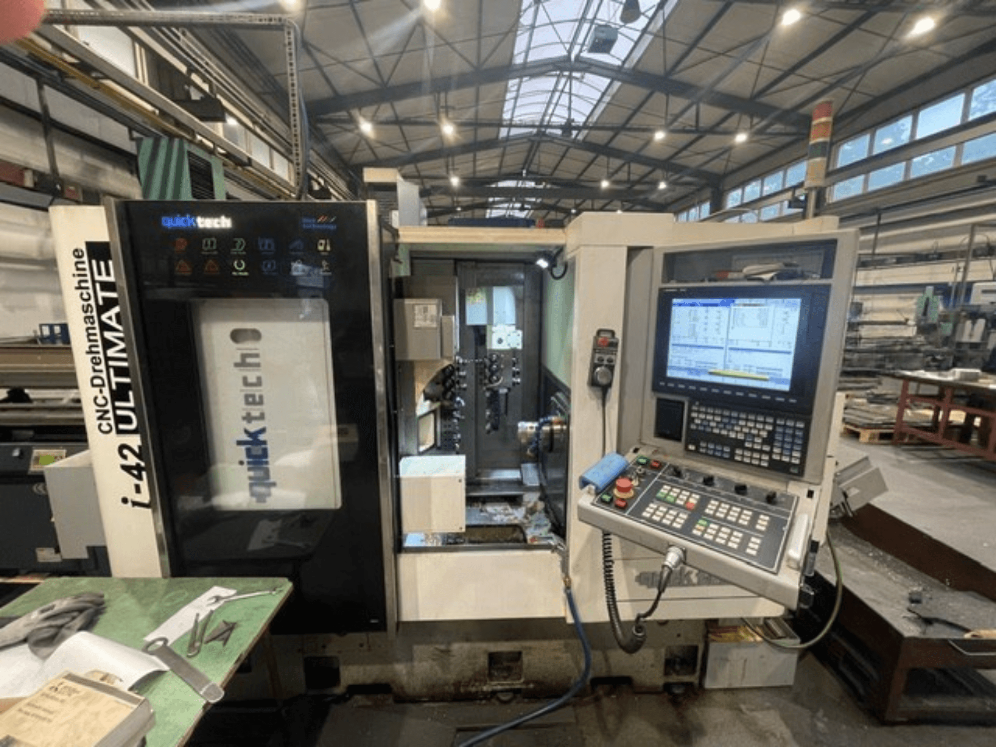 Máquina de torneado tipo suizo Quick-Tech I-42U, vista frontal, mostrando el panel de control y la interfaz CNC en un entorno de taller.