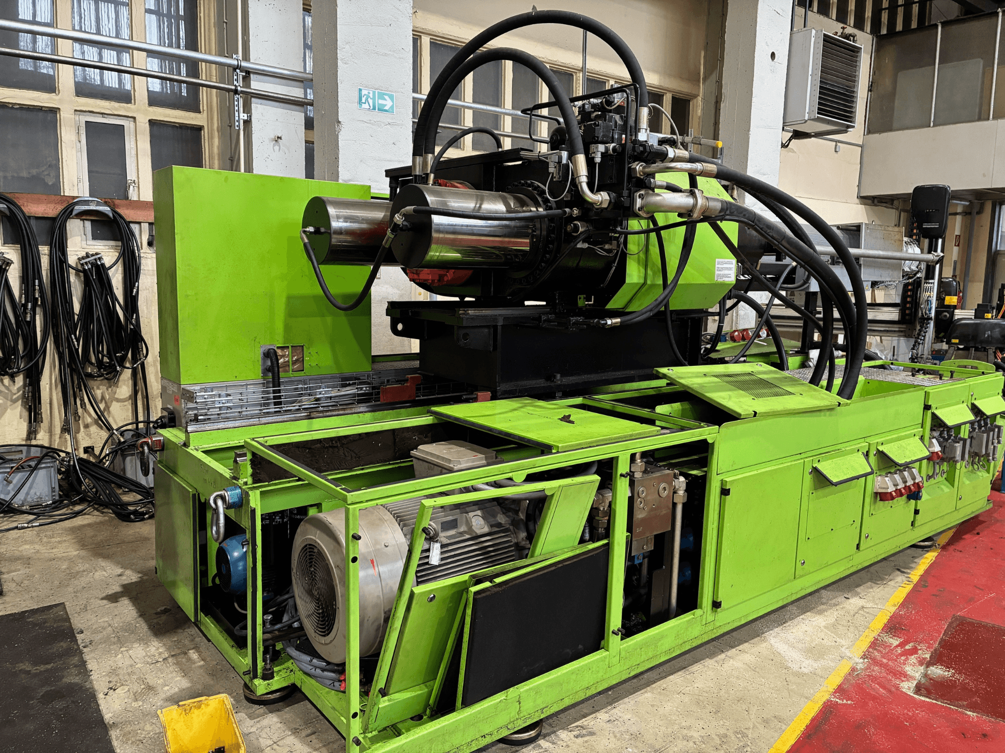Máquina industrial verde con sistema hidráulico, vista frontal, mostrando el motor y varios paneles de control.