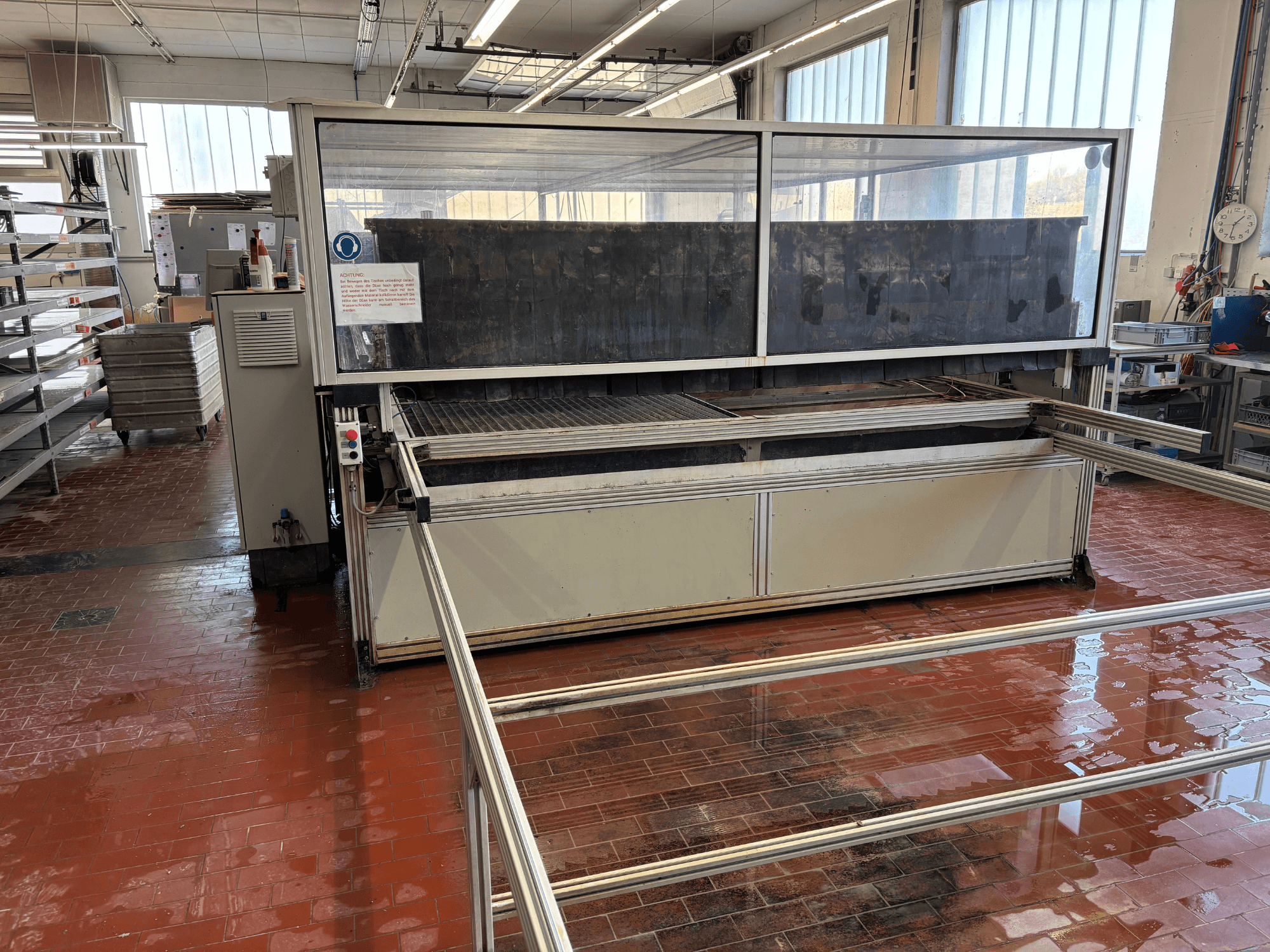 Máquina de corte por chorro de agua EXPERT SYSTEMTECHNIK «cutExpert variojet» en un taller, vista frontal, con una gran cubierta transparente.